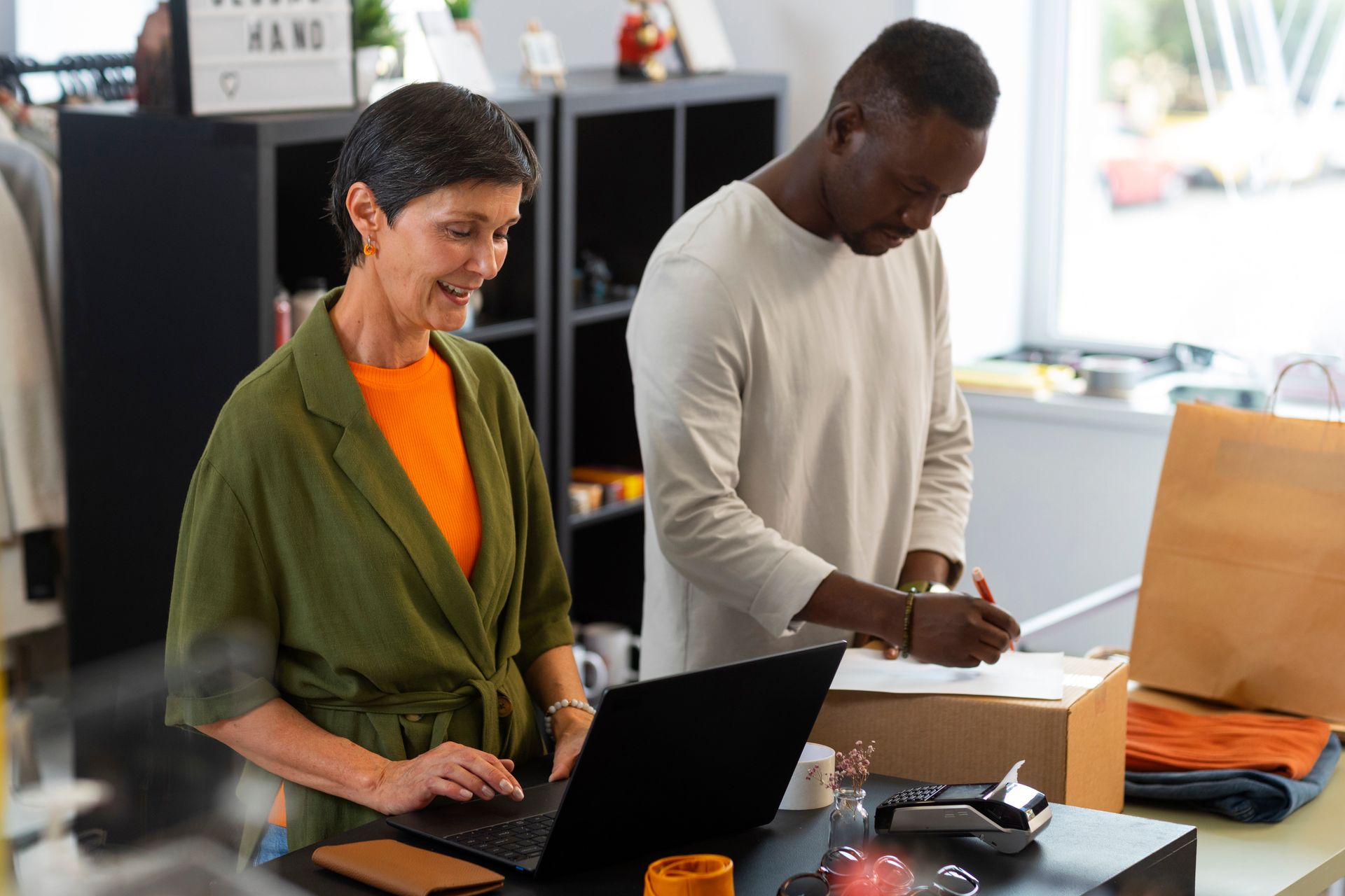 Woman and man reviewing documents at a desk in an office with plants and a computer.