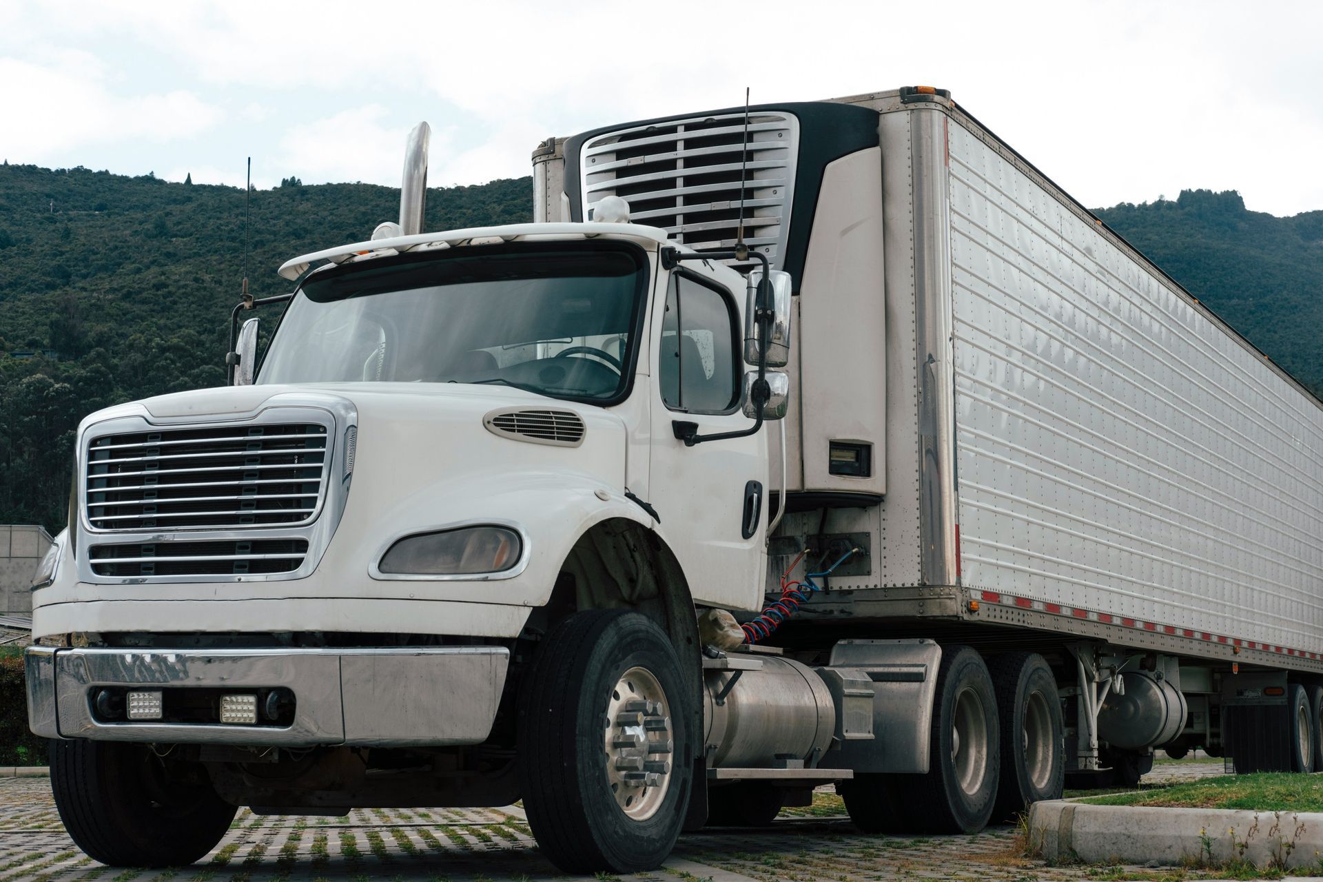 White semi-truck parked outdoors on a road with green hills in the background