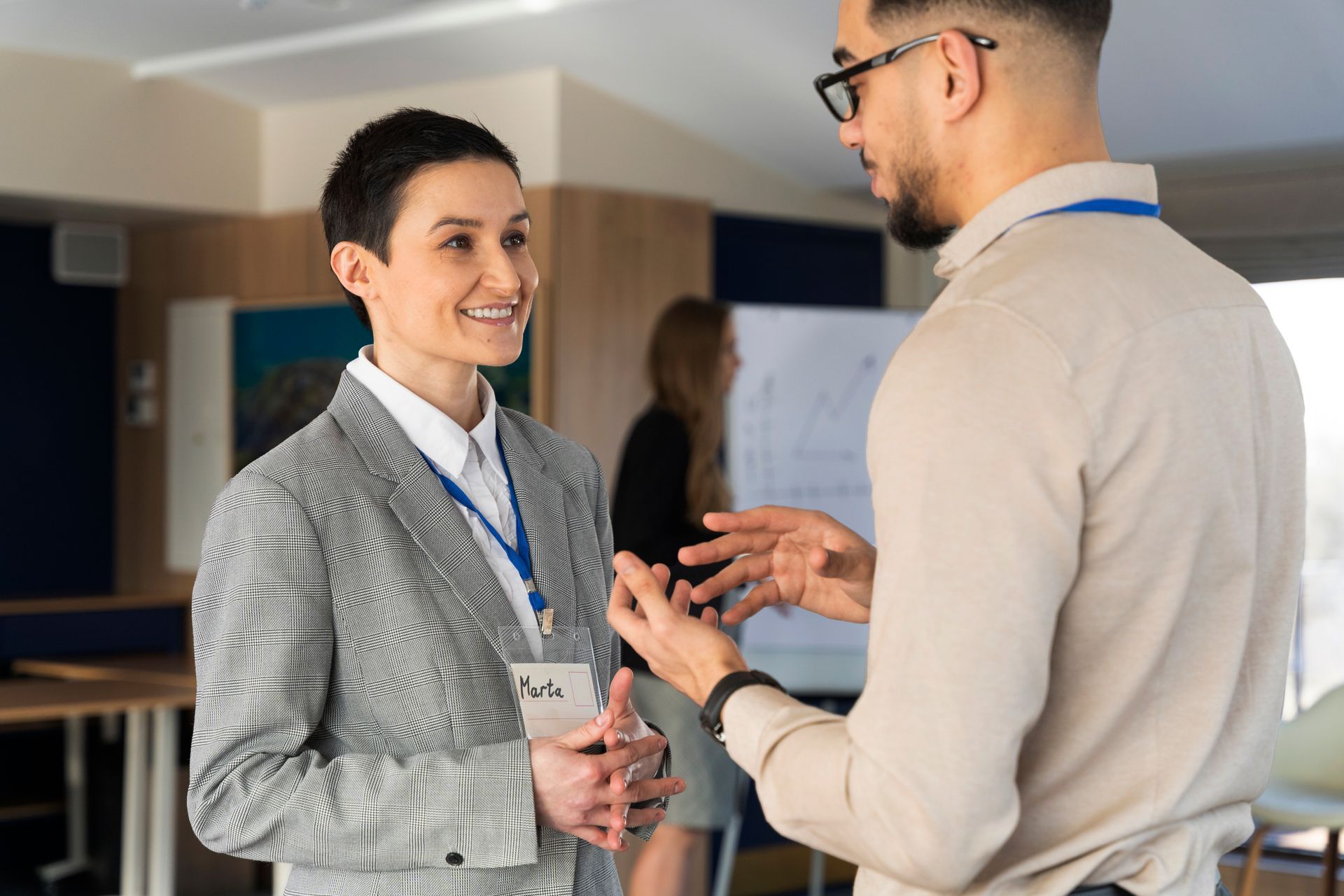 Two coworkers in business attire chatting and smiling at a conference or office event.