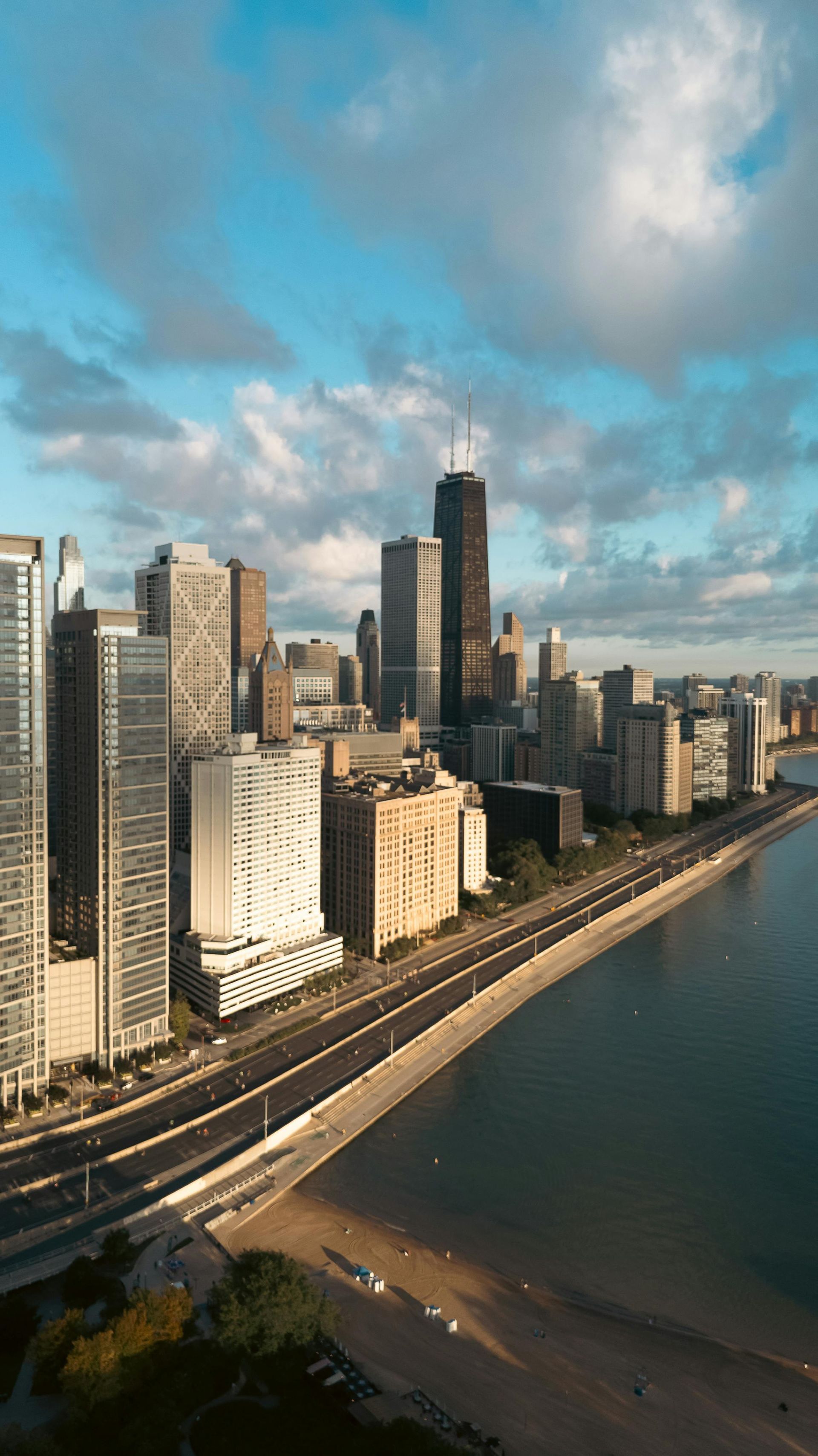 City skyline with tall buildings along a waterfront under a cloudy blue sky.