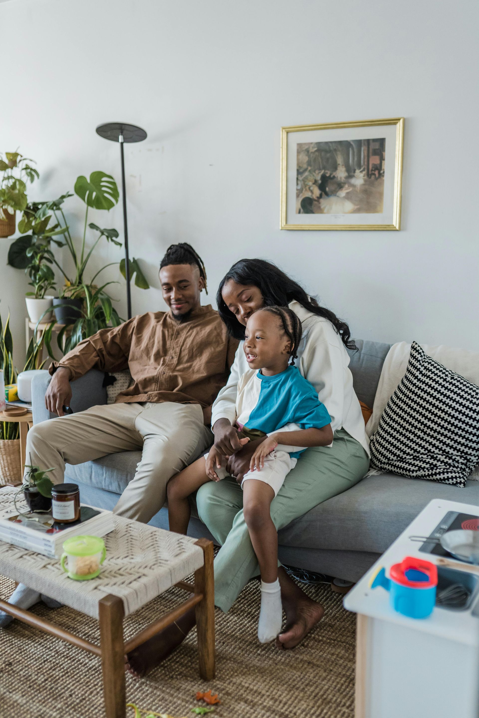 Three people sitting together on a couch in a bright living room, smiling and relaxing.