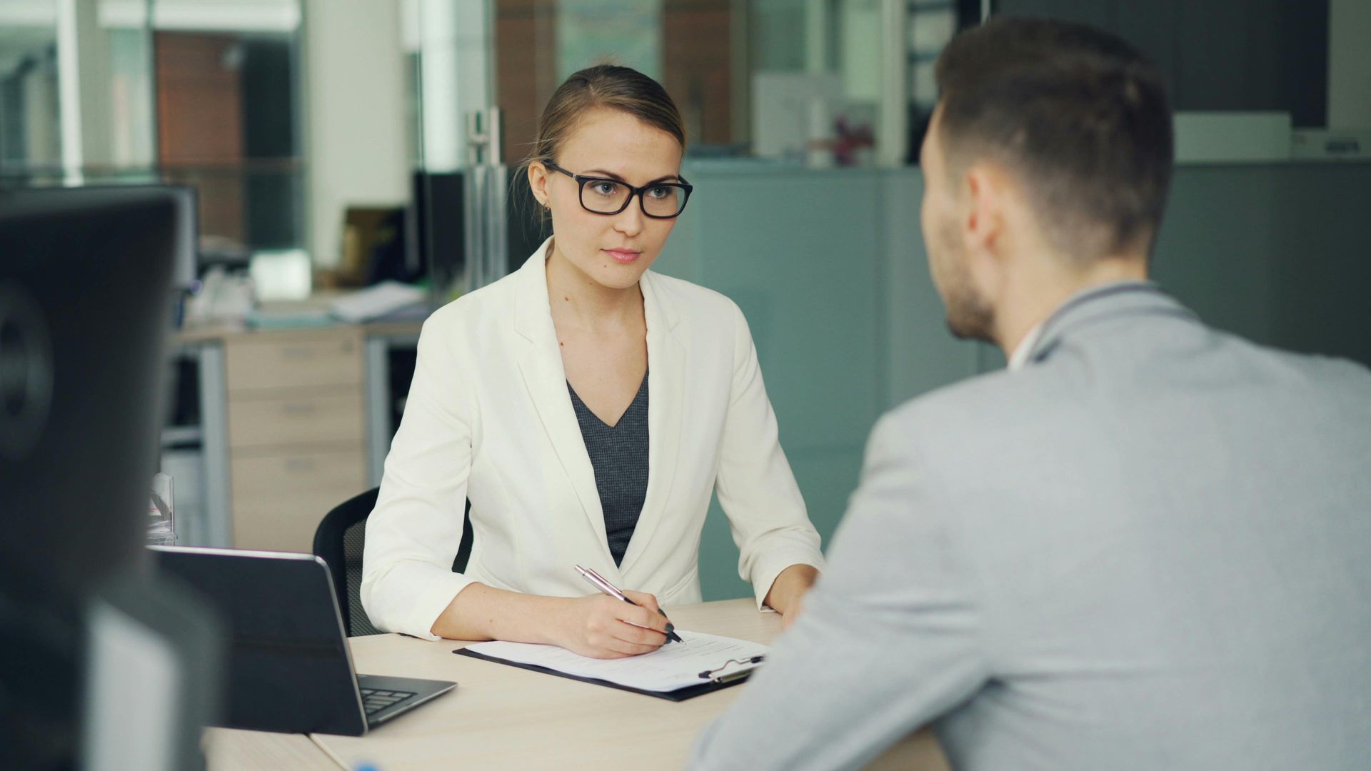 Woman and man reviewing documents at a desk in an office with plants and a computer.