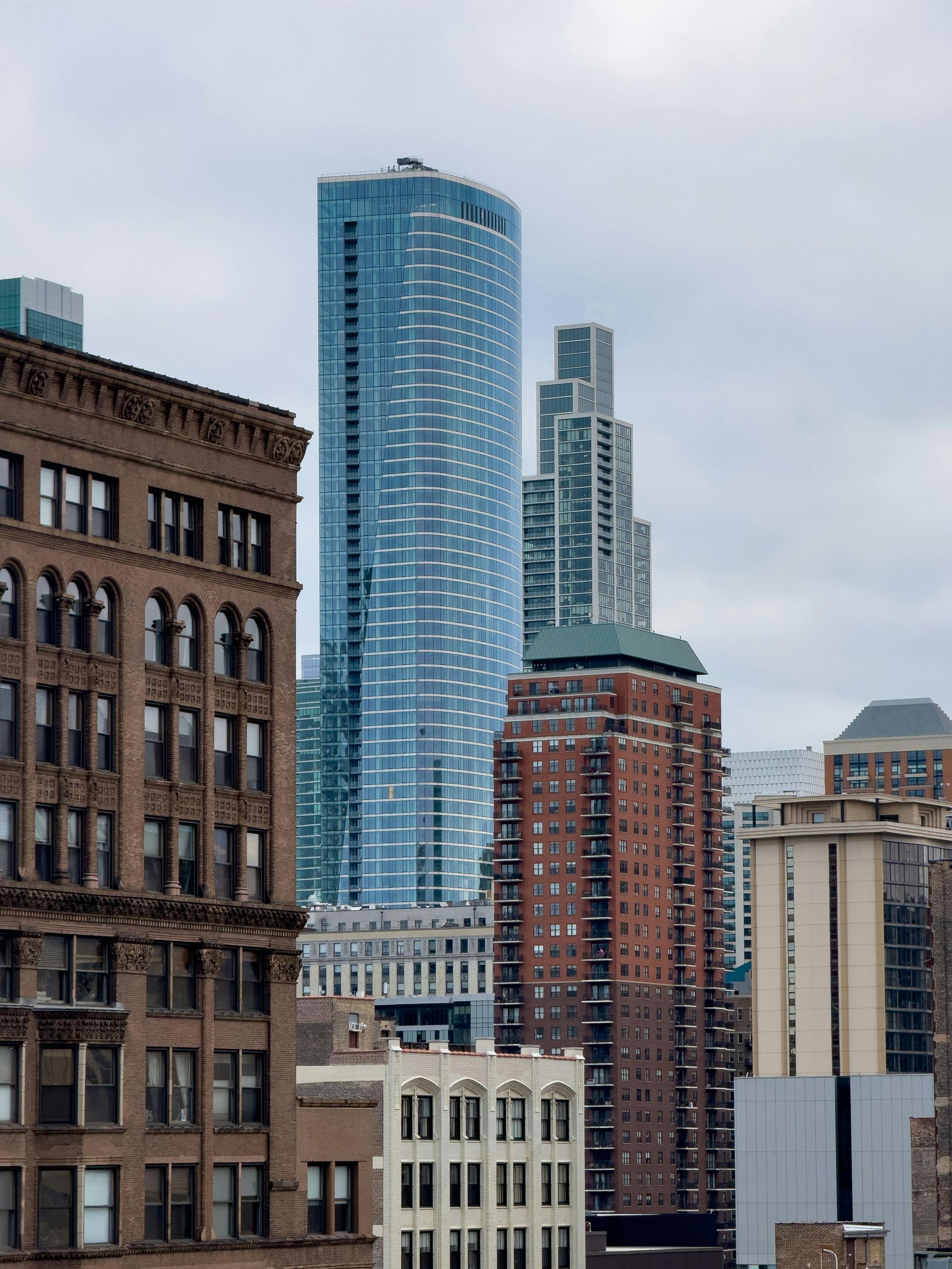 Downtown city skyline with tall modern glass and brick buildings under a cloudy sky