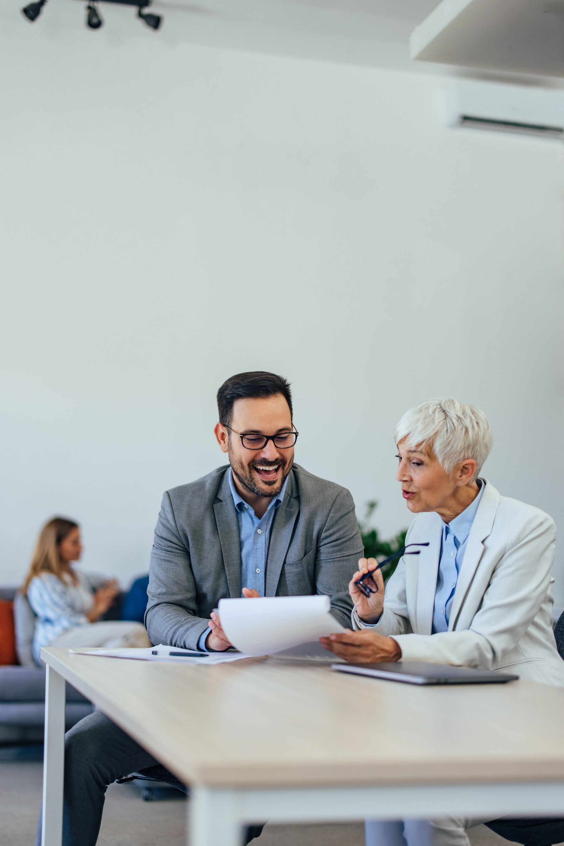 Two colleagues smiling and discussing a document at a table in a bright office