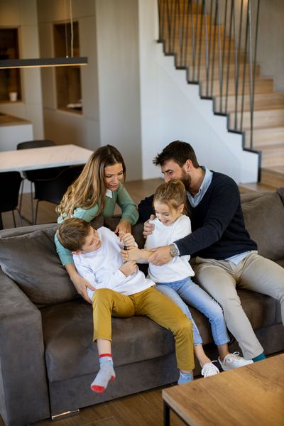 Family sitting on a gray sofa, reading together in a bright living room near a staircase