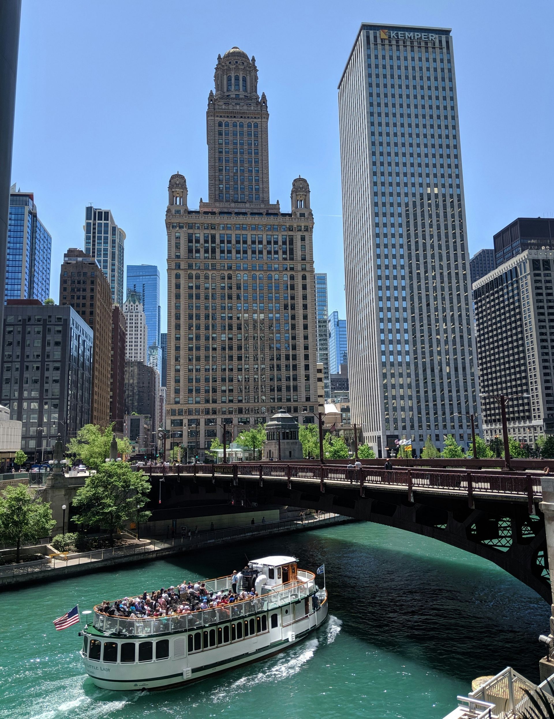 Tour boat on a river beneath a bridge, with Chicago skyscrapers and a clear blue sky in the background