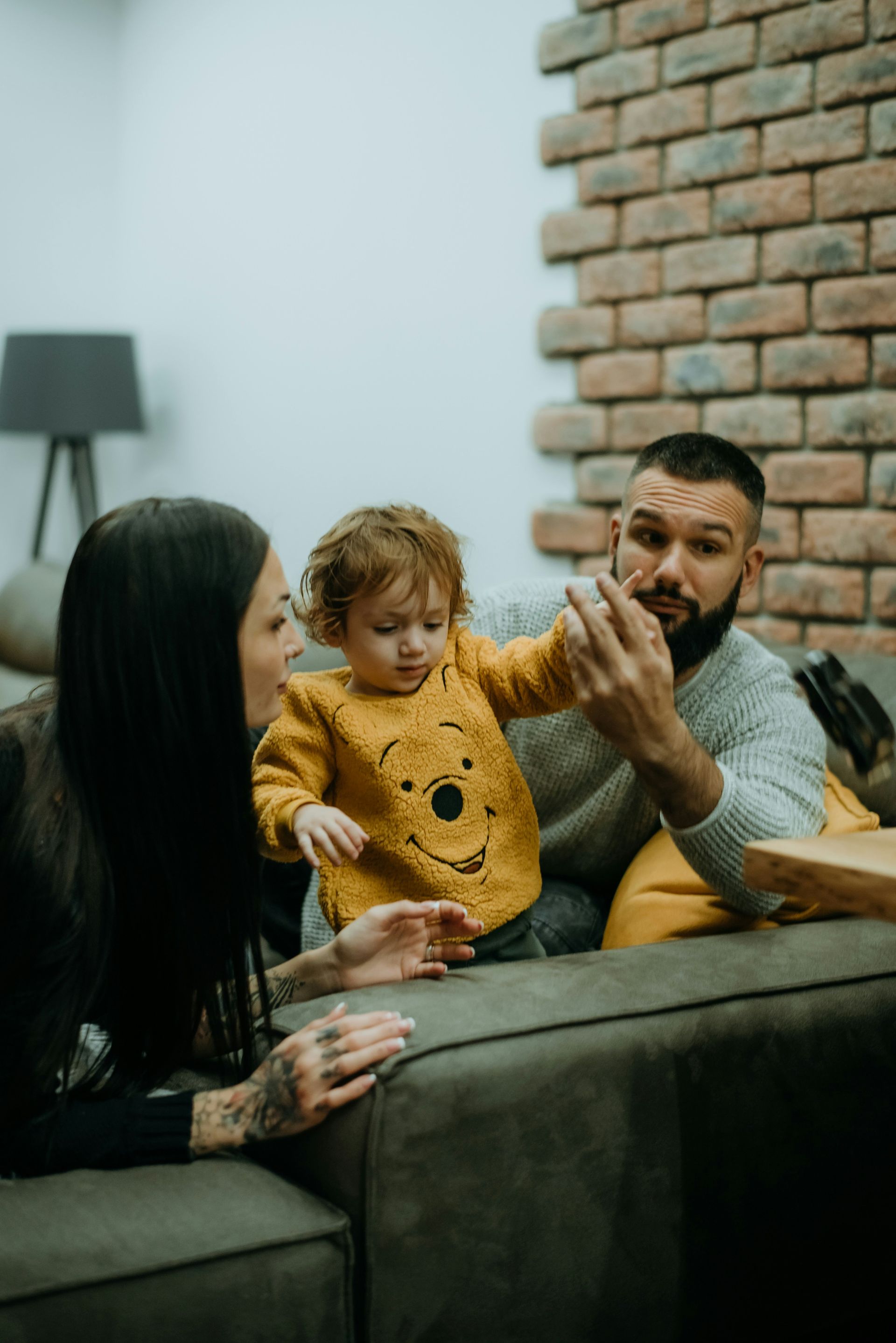 Family sitting on a couch, holding a baby in a yellow sweater in a cozy living room.
