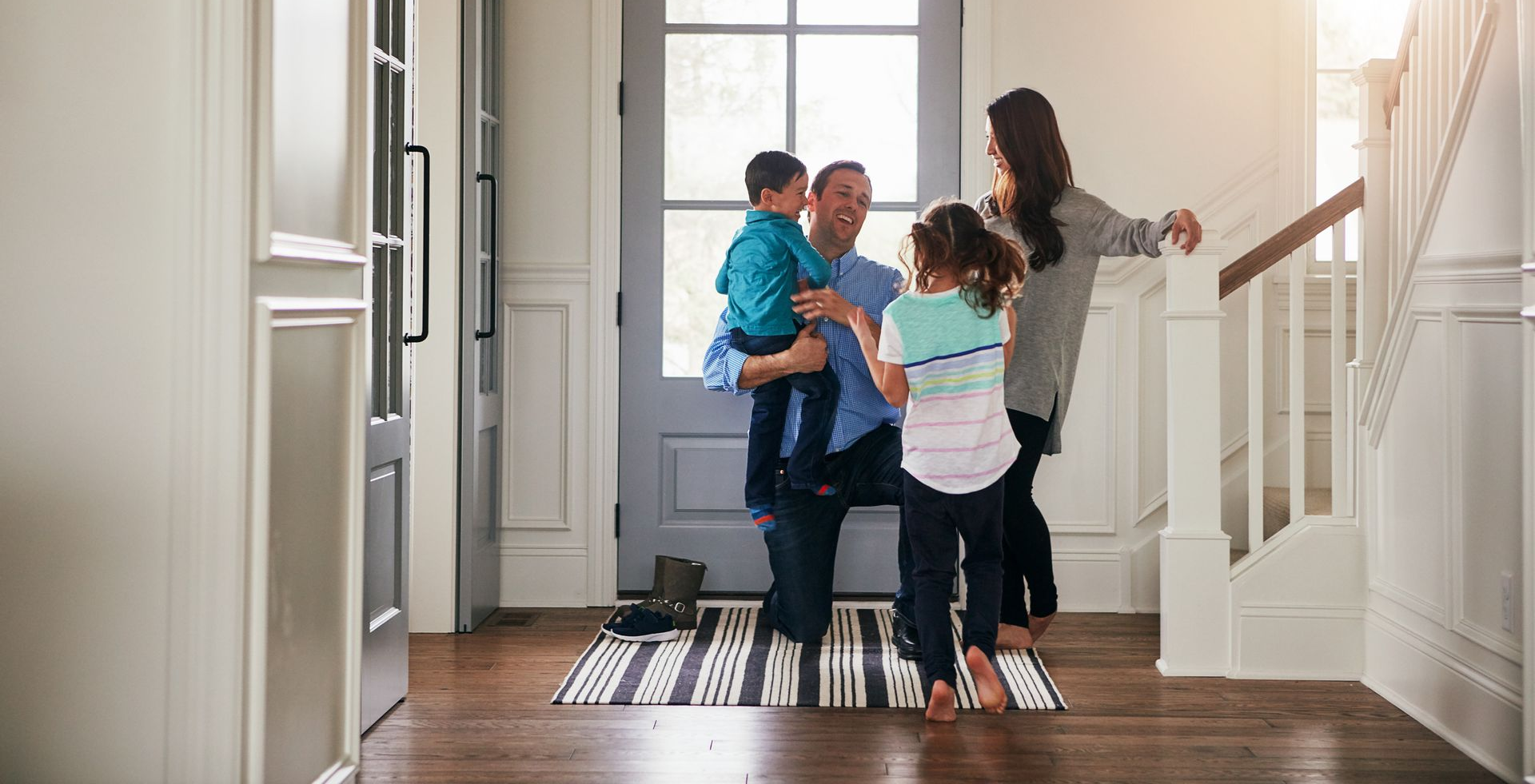 Family embracing in a bright entryway beside a front door and staircase