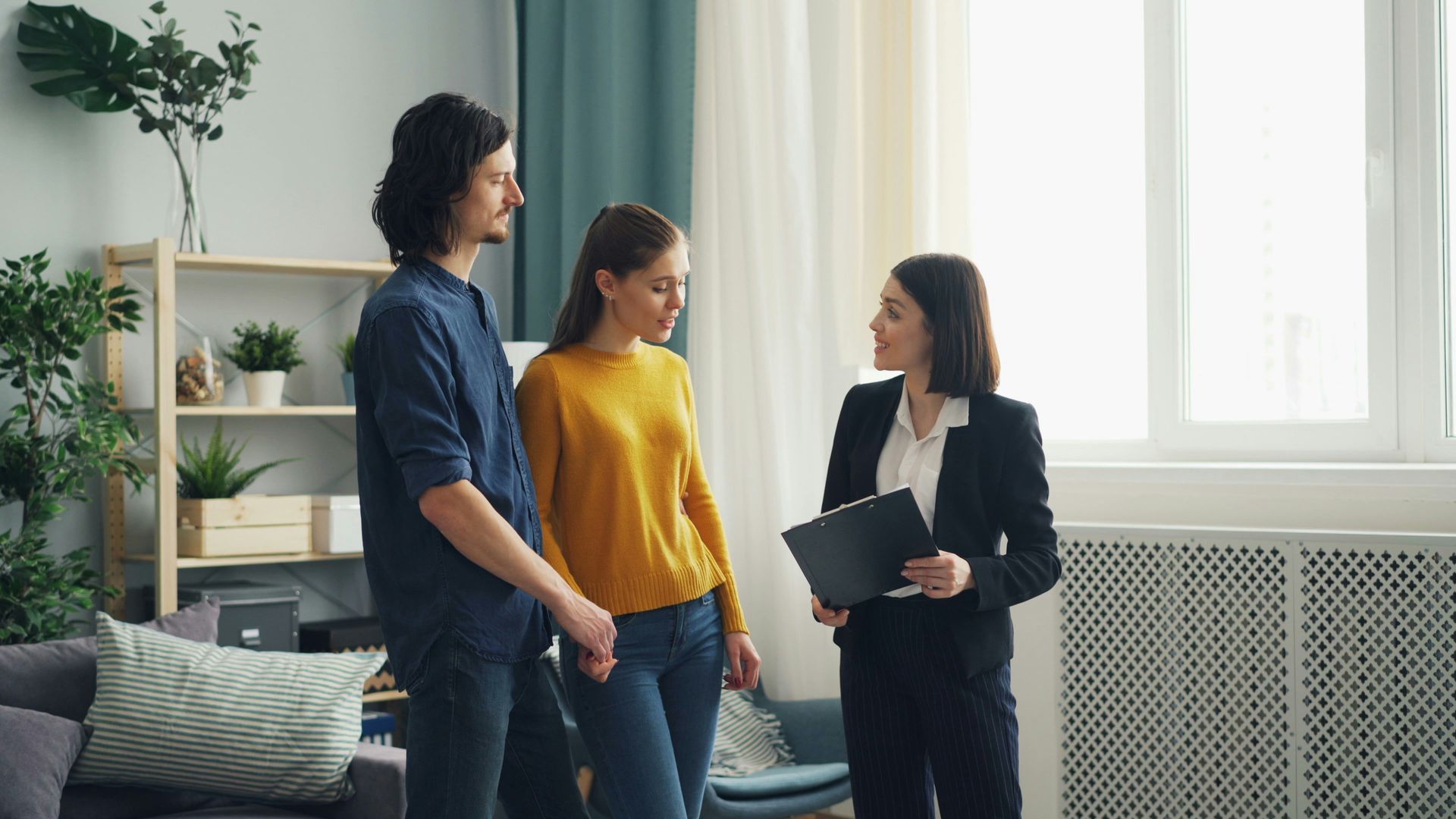 Three people talking in a bright living room, one holding a folder.