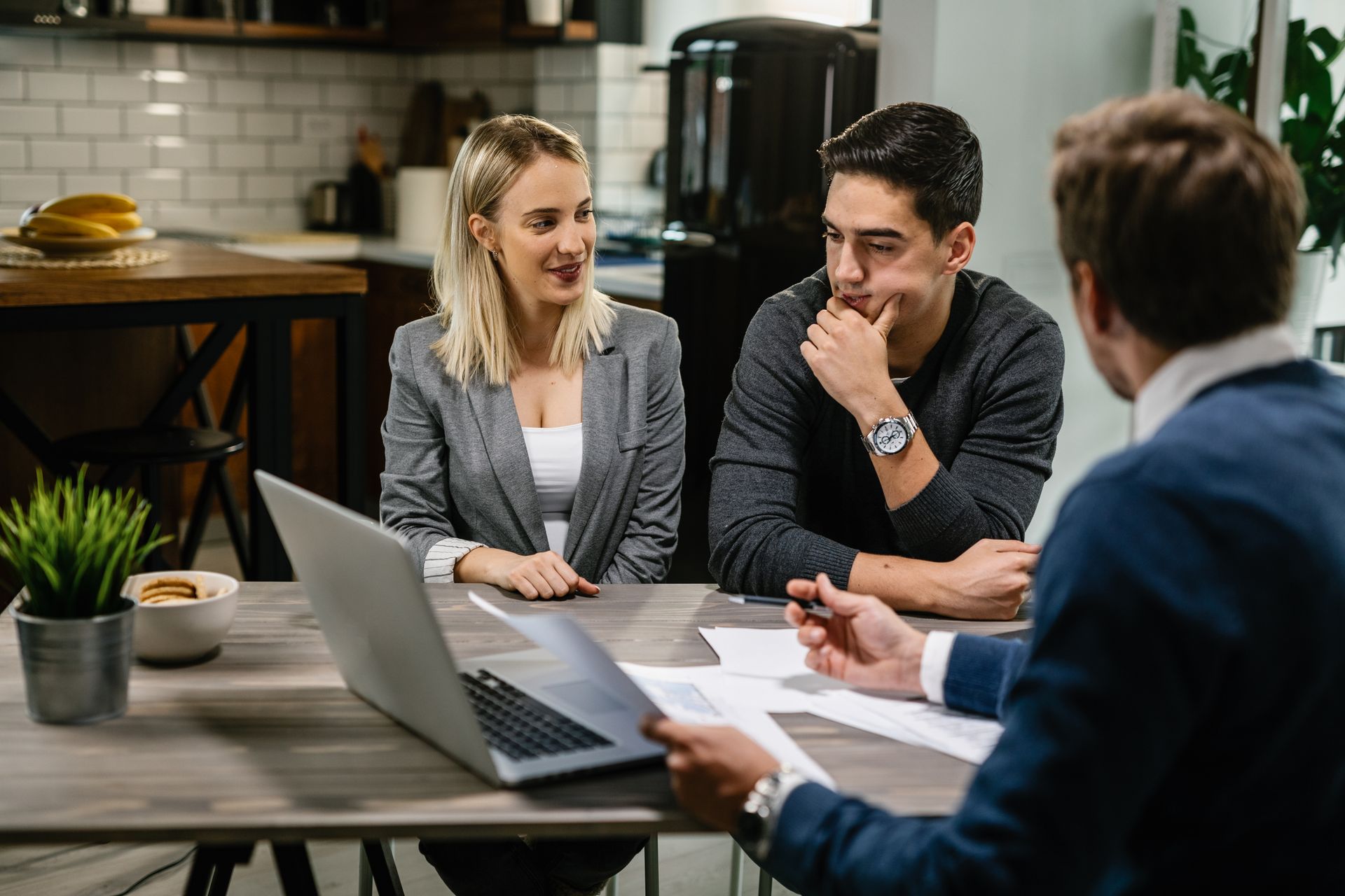 Three coworkers meeting around a laptop at a table in a modern office.