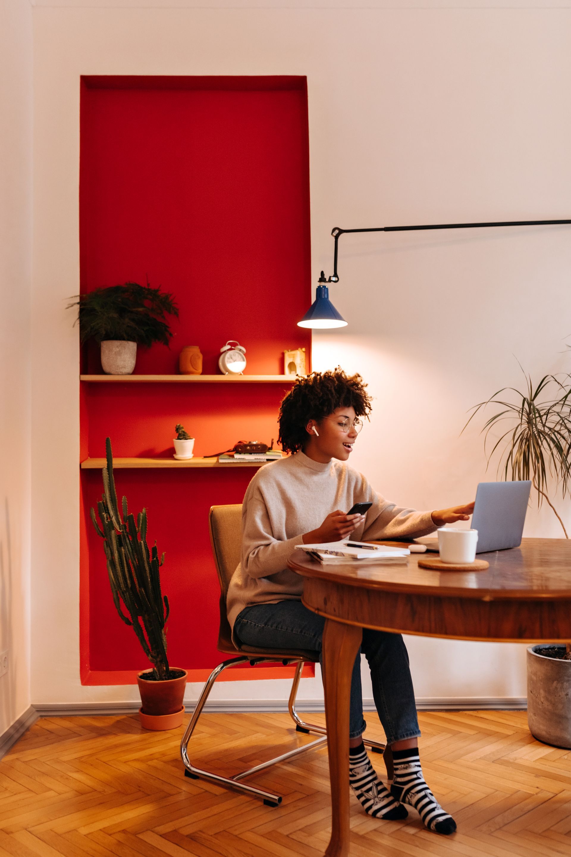 Person working at a round wooden table in a bright room with a red alcove and laptop
