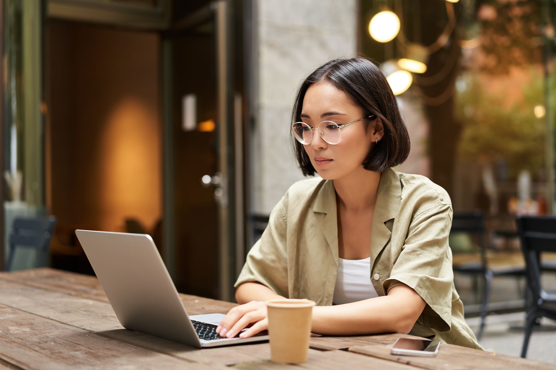 Person working on a laptop at an outdoor café table with a coffee cup nearby