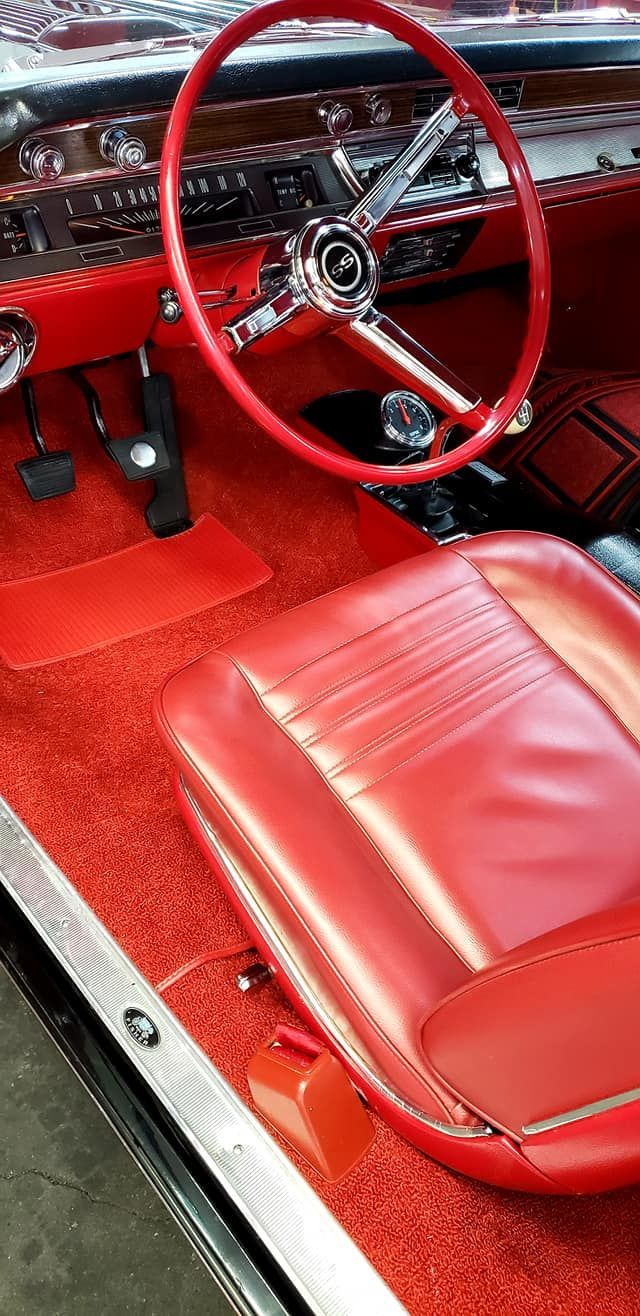 Red interior of a classic car, showing steering wheel, seat, and carpet.