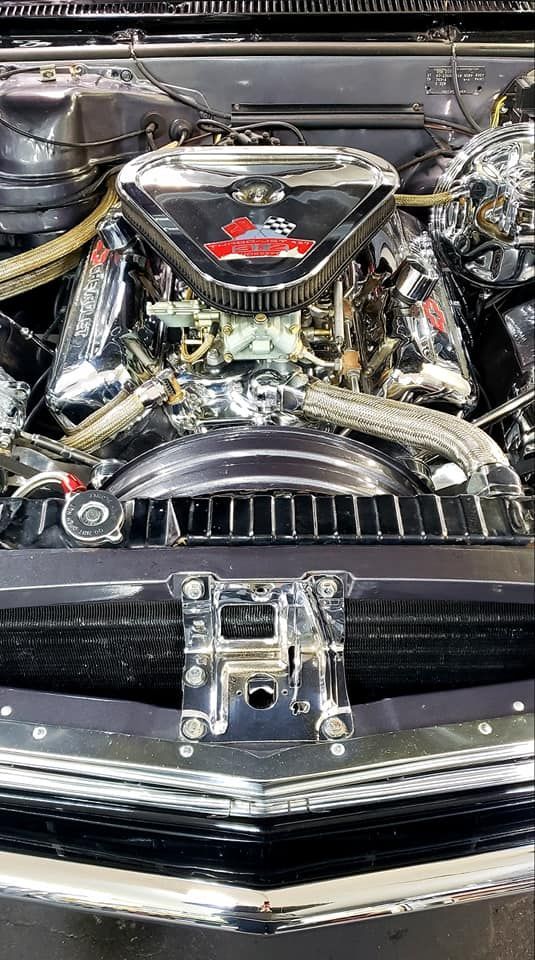 Shiny chrome engine bay of a classic car, including the air filter, carburetor, and radiator.