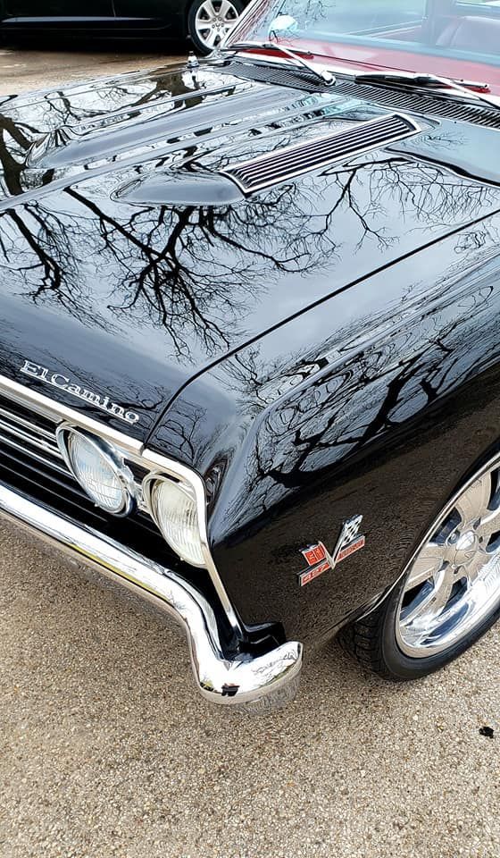 Black classic car with chrome details reflecting trees. 