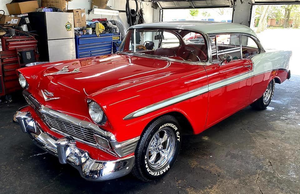 Red and white 1956 Chevrolet Bel Air classic car in a garage with tools in the background.