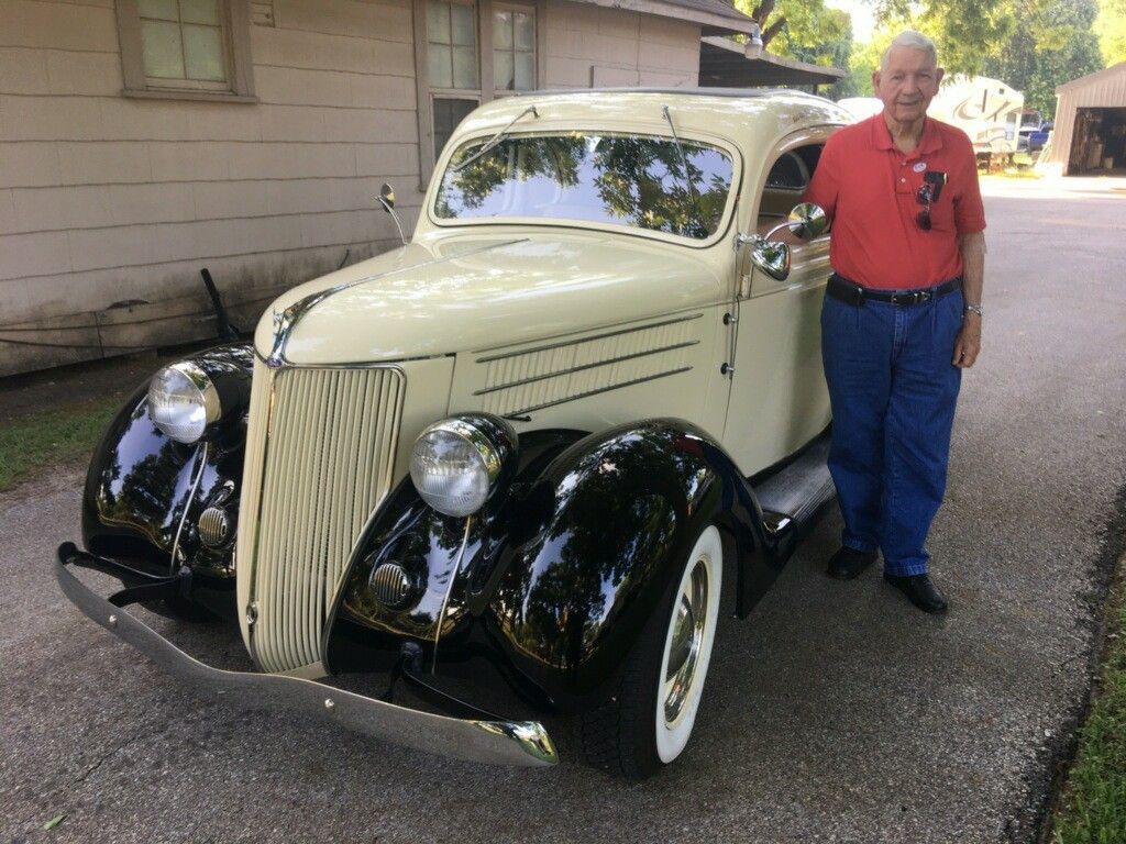 Man standing next to a vintage, cream-colored car with black fenders.