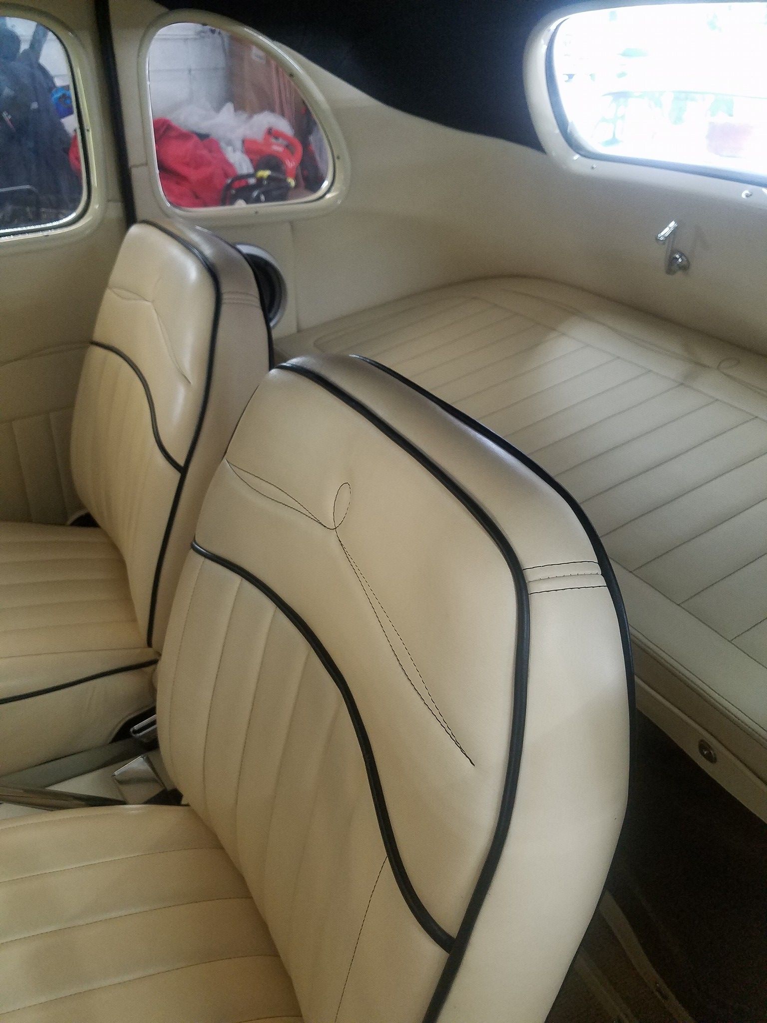 Interior view of a cream-colored car with black trim on the seats and a backseat.