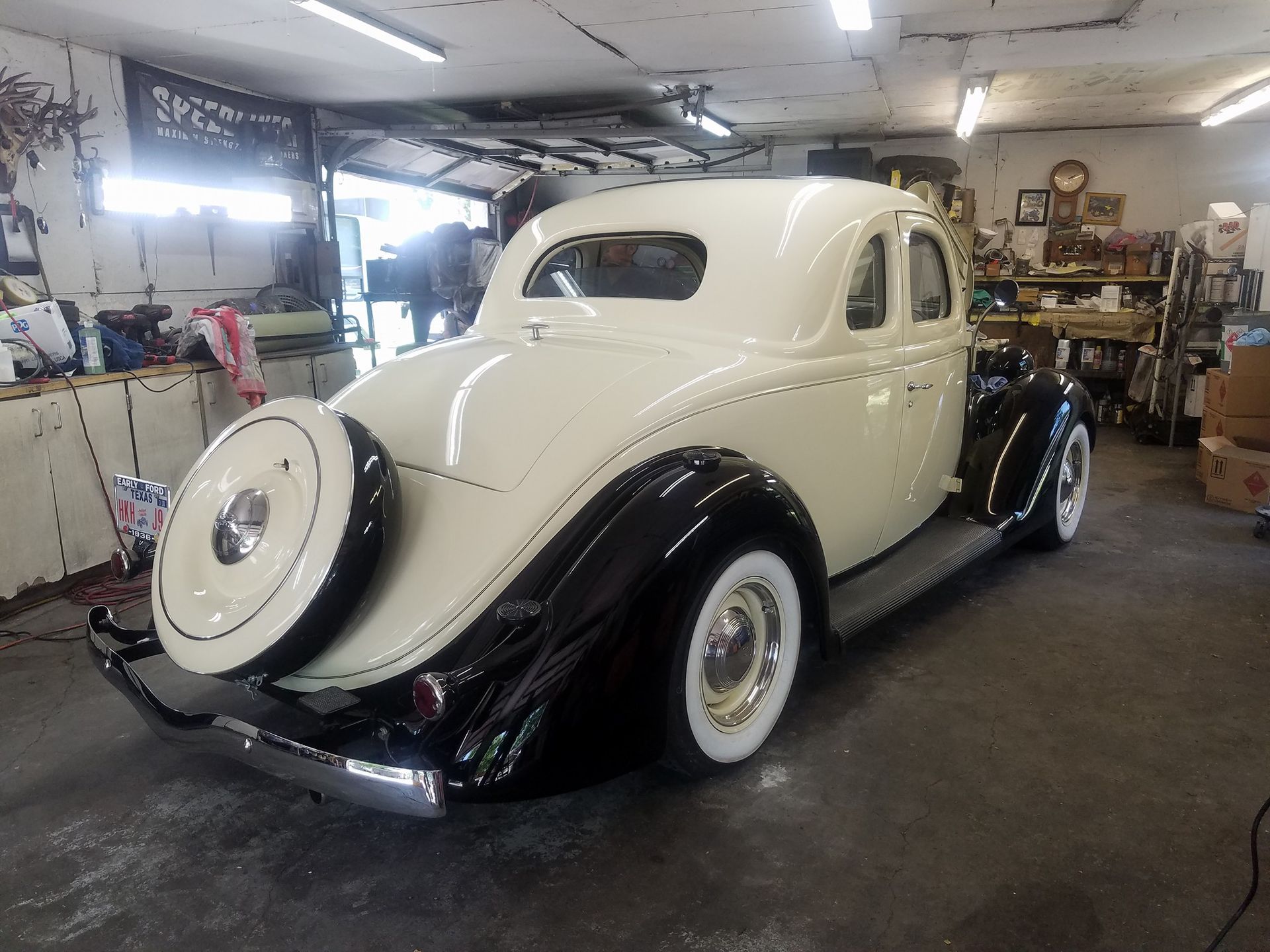 Cream and black vintage coupe, spare tire on back, parked in a garage.