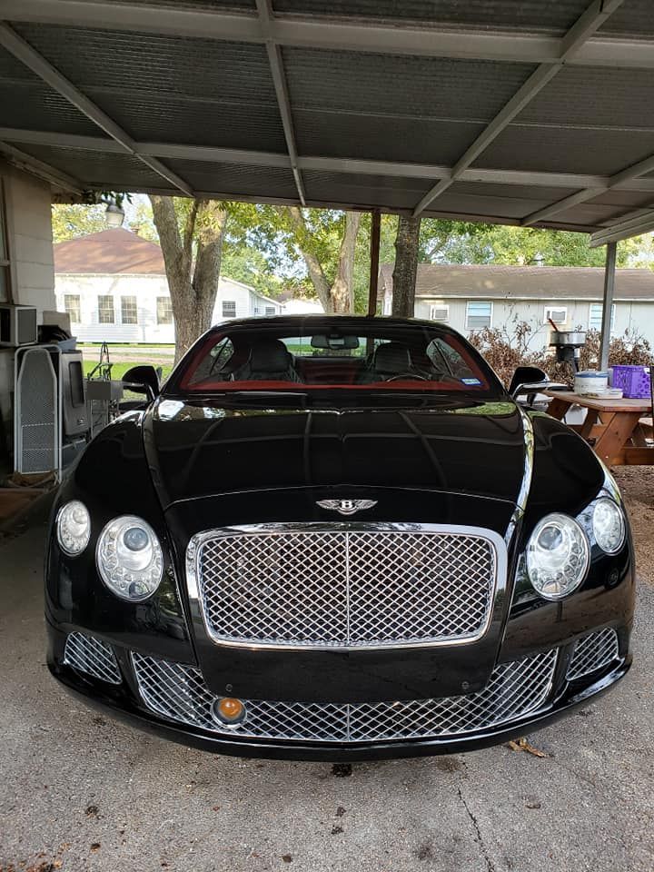 Black Bentley car with chrome grill parked under a carport.