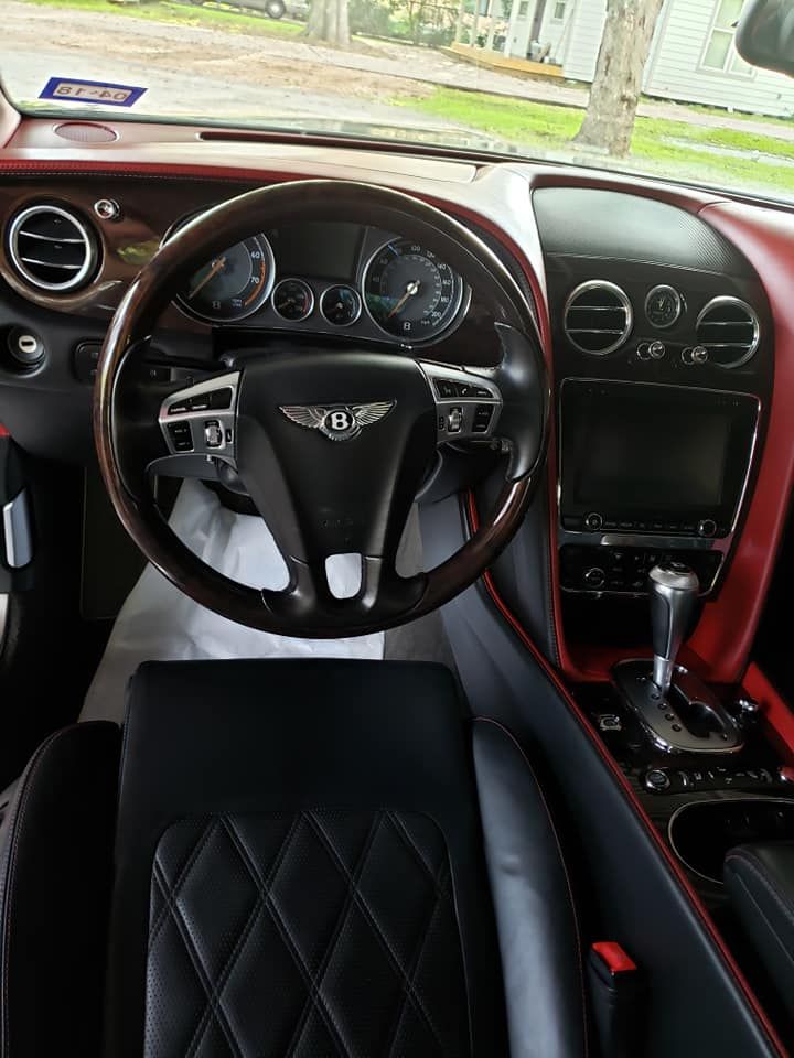 Bentley car interior, red and black leather, wood trim, steering wheel, dashboard with gauges and screen.