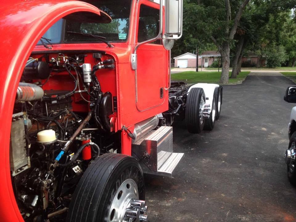 Red semi-truck cab with open hood, engine visible, parked on asphalt driveway.