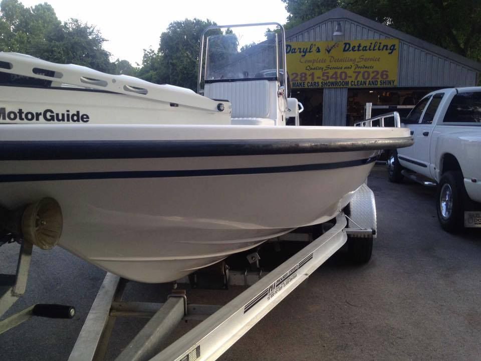 White boat on a trailer, with a MotorGuide logo. A white truck and a detailing shop are visible in the background.