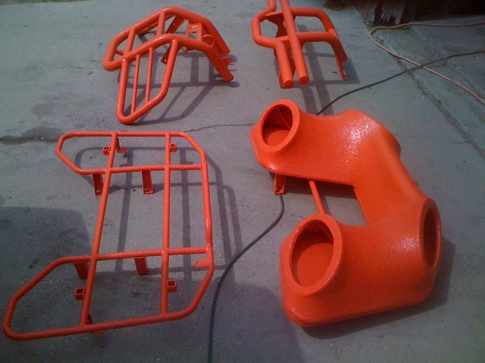 Four bright orange ATV parts resting on a gray surface.