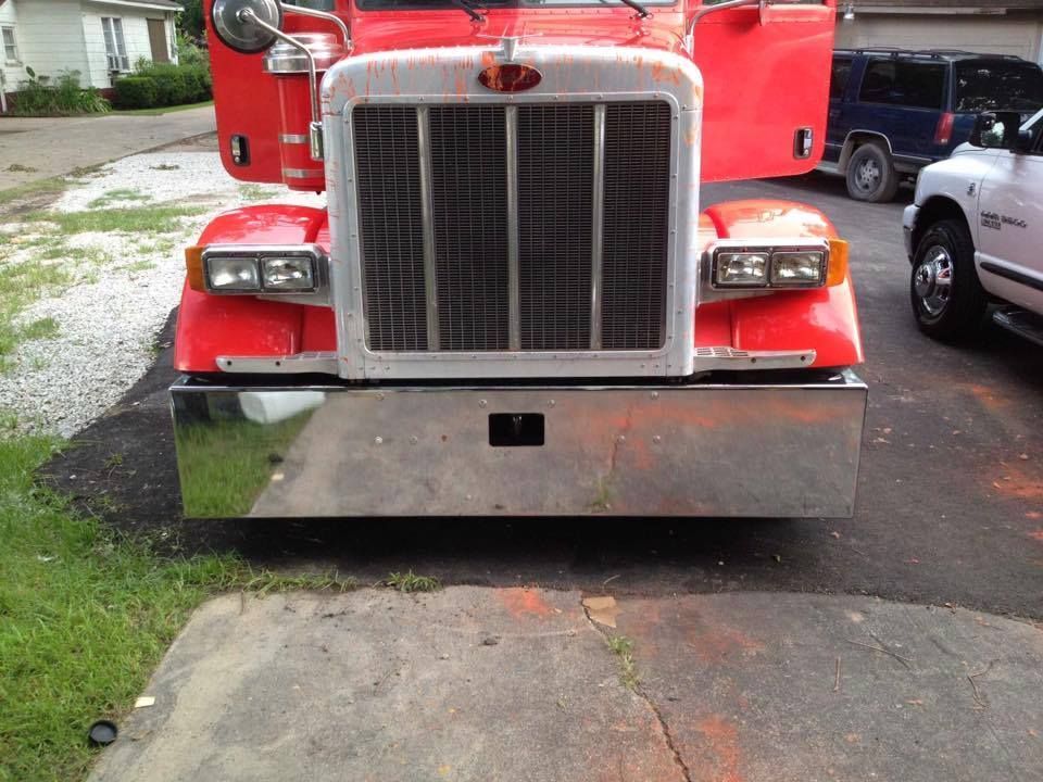 Red Peterbilt semi-truck with chrome bumper and open doors, parked in a driveway.