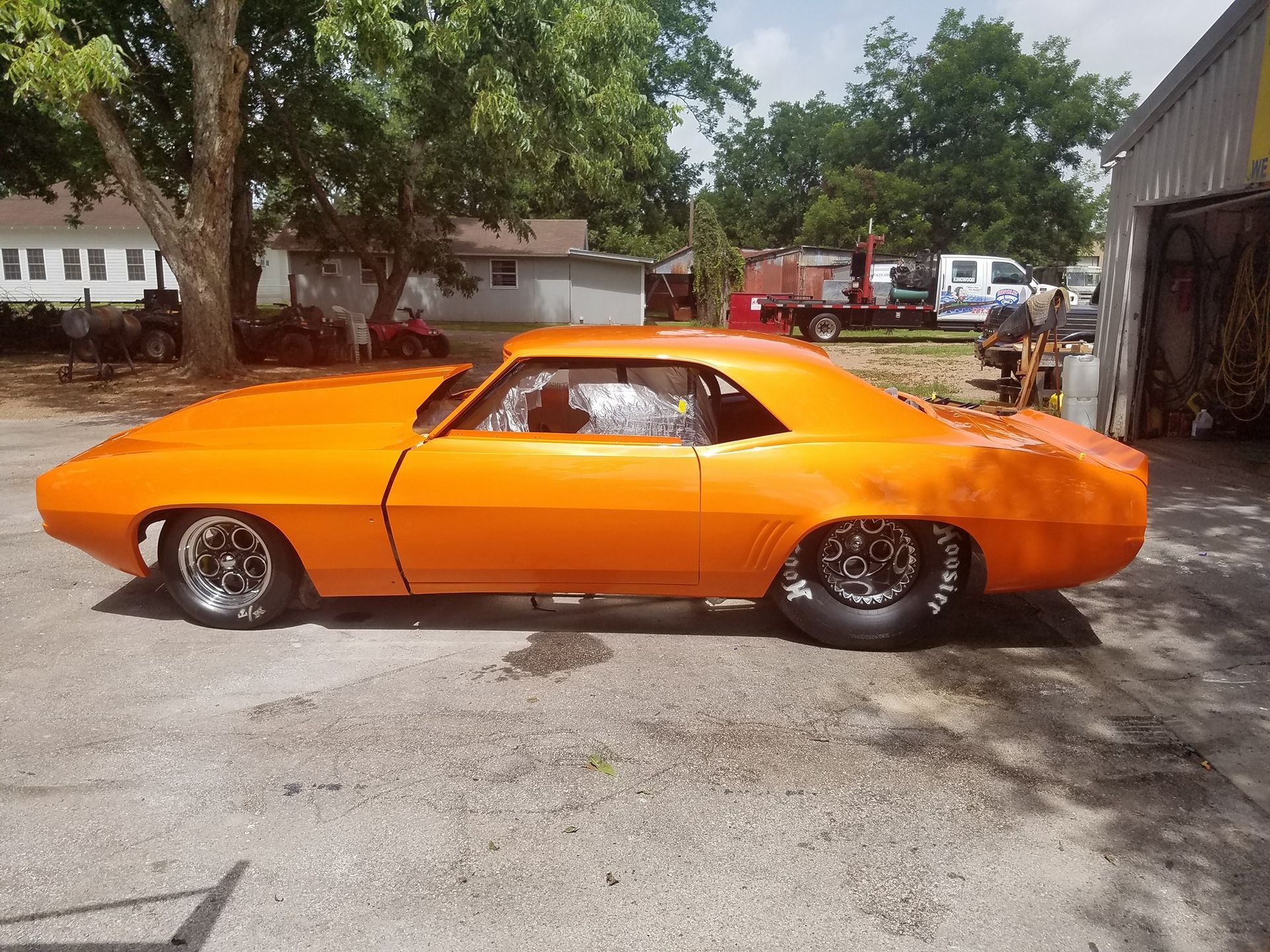 Bright orange classic muscle car, possibly a Camaro, parked outside on pavement.