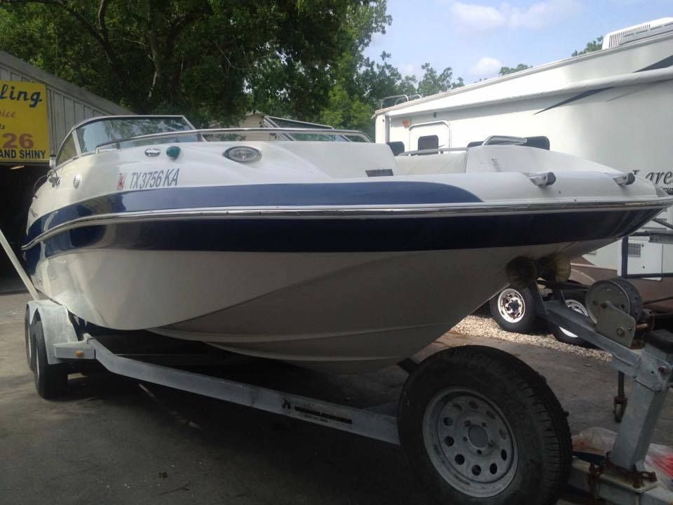 White and blue motorboat on a trailer, parked outside a building.