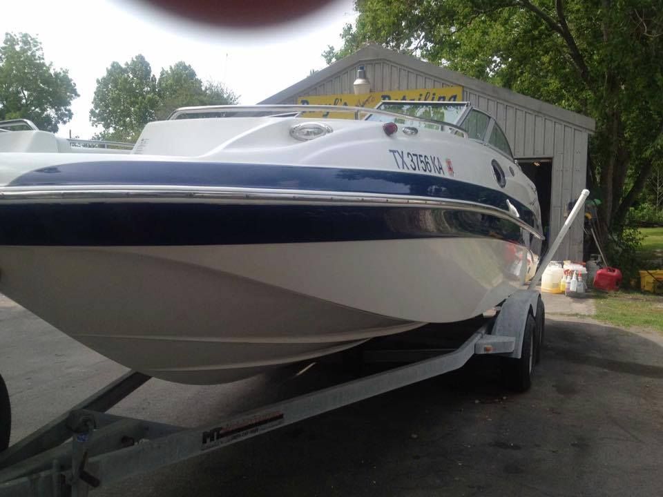 White and blue boat on a trailer parked outside a building.