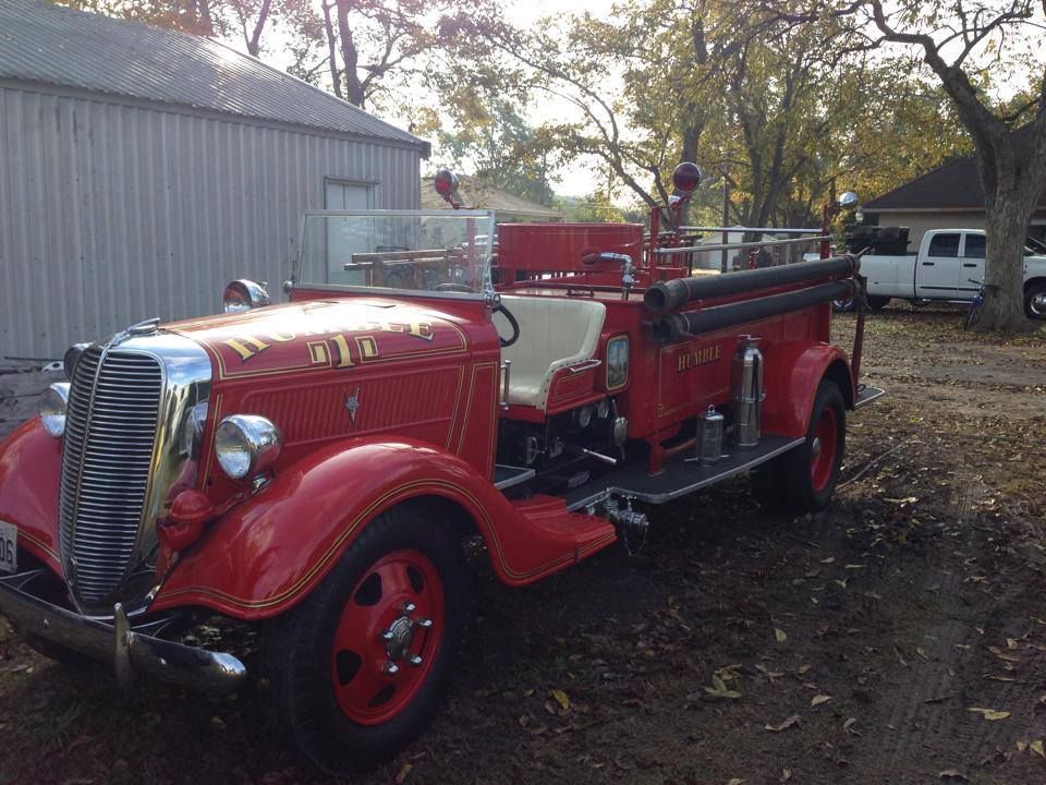 Red vintage fire truck parked outdoors near a building and trees.