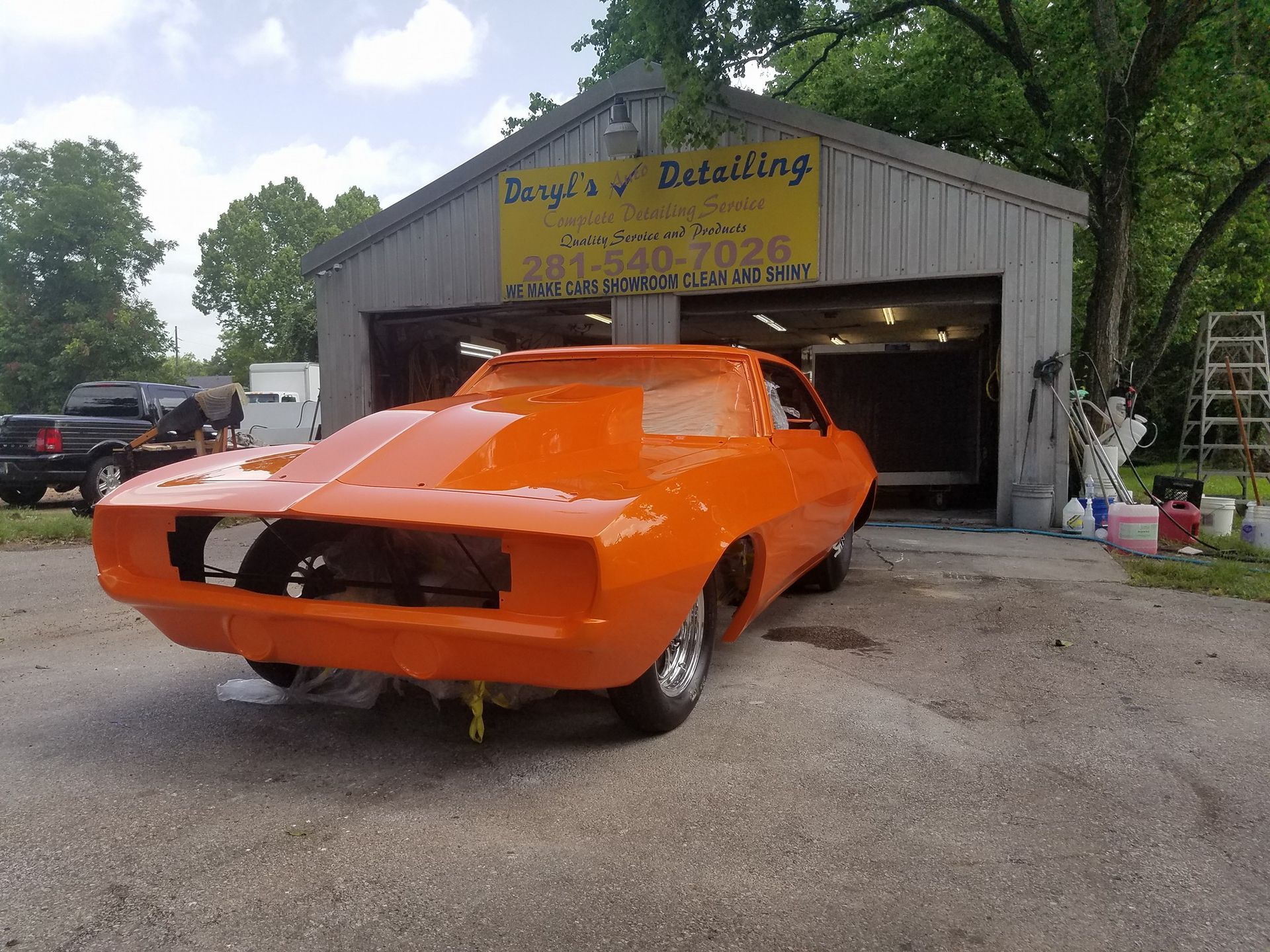 Orange muscle car in front of a detailing shop with open garage.
