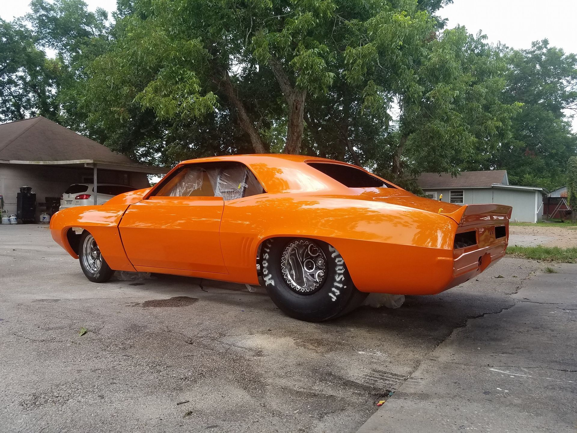 Orange drag racing car, rear view, parked on pavement.
