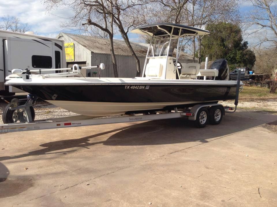 Black and beige motorboat on a trailer, with a white roof and fishing rod holders, parked outside.