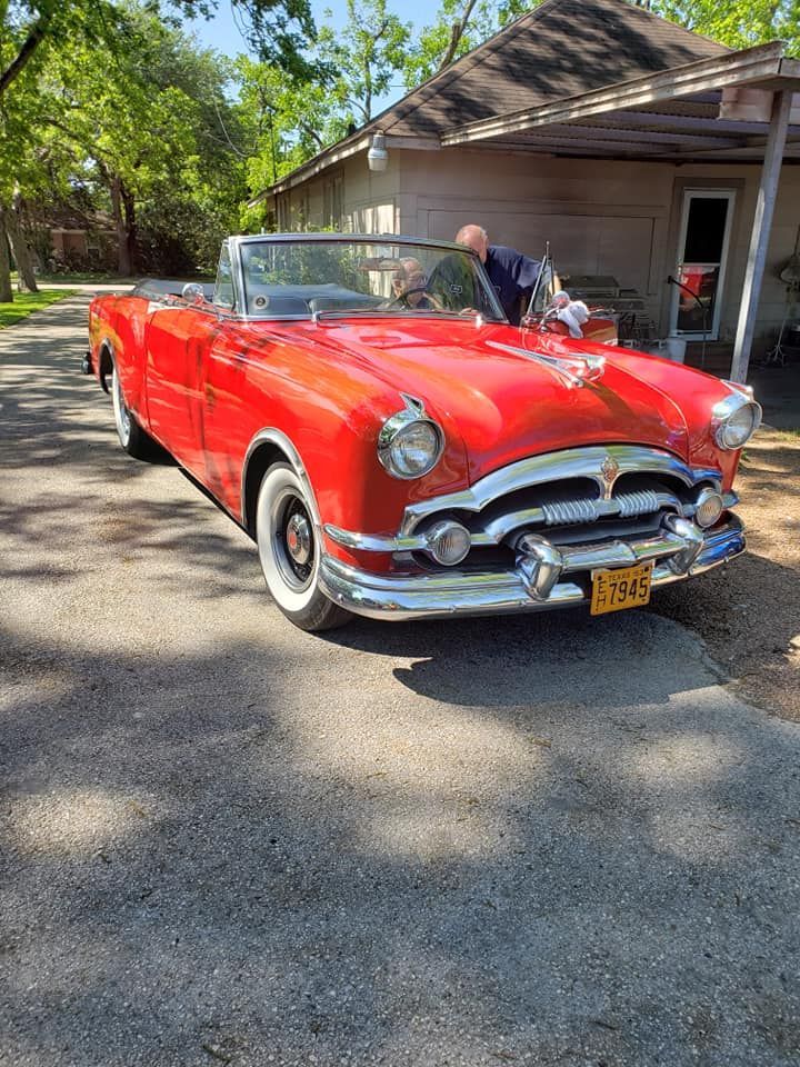 Red classic convertible car parked on a paved driveway in front of a building.