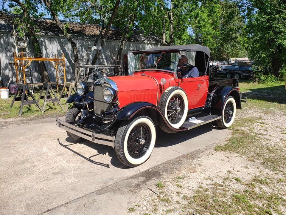 Red antique Ford Model A convertible with white-walled tires, parked outside on a sunny day.