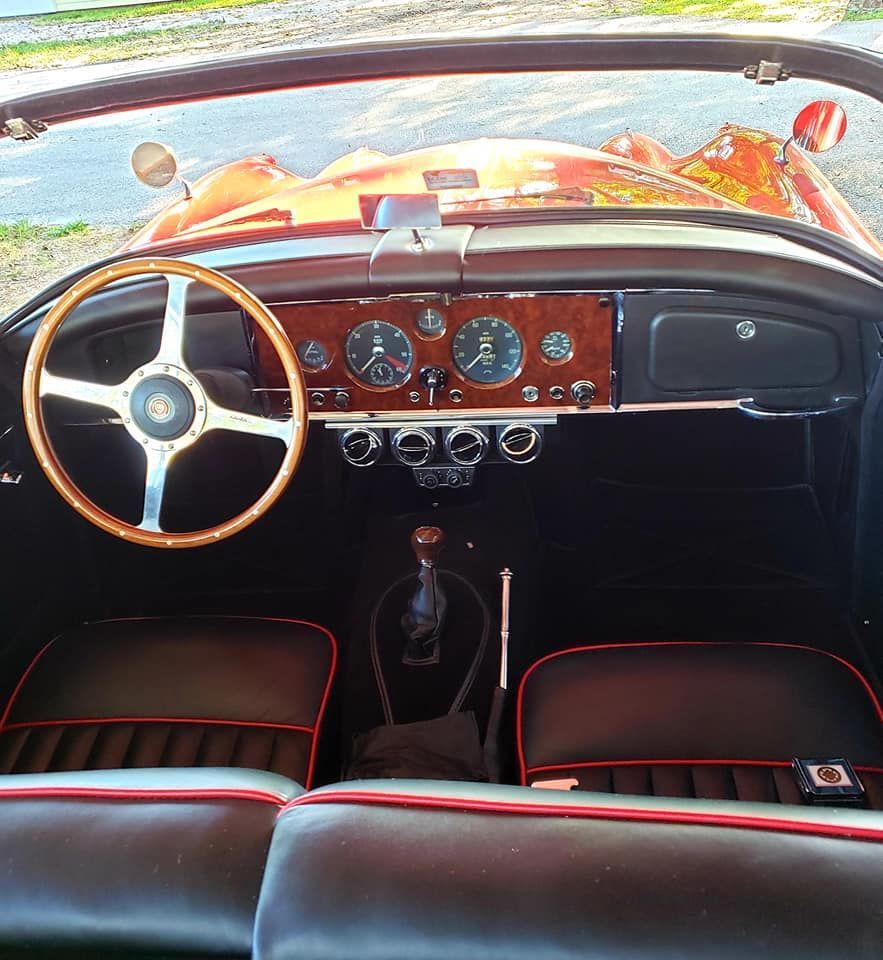 Interior view of a classic red convertible car; wooden steering wheel, black seats with red trim, wooden dashboard.