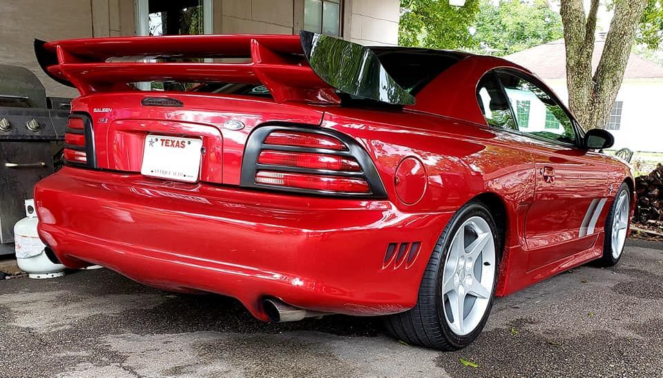 Red Ford Mustang with large spoiler, parked outside.