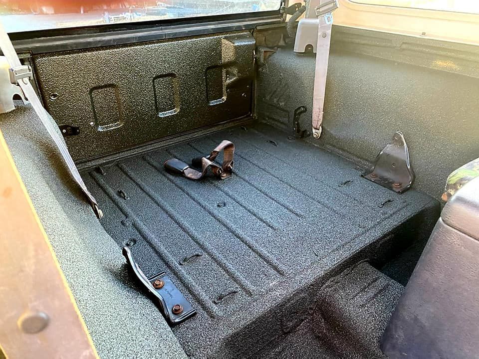Black bed of a vehicle with textured liner, seatbelt, metal pieces.