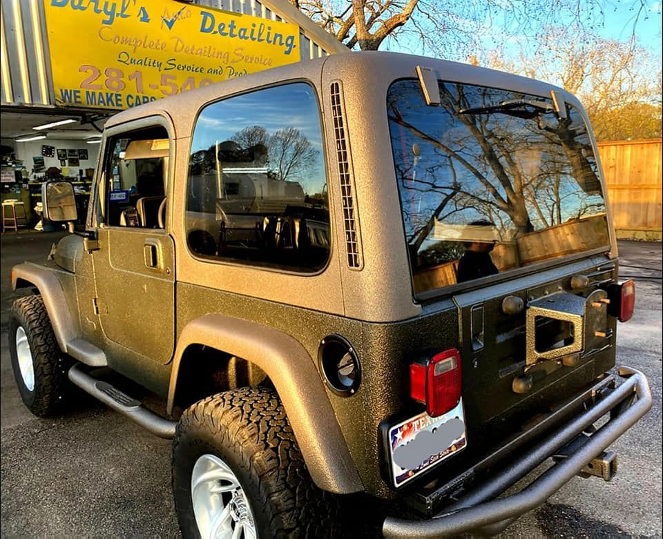 Olive green Jeep Wrangler with a tan hardtop parked in front of a detailing shop.