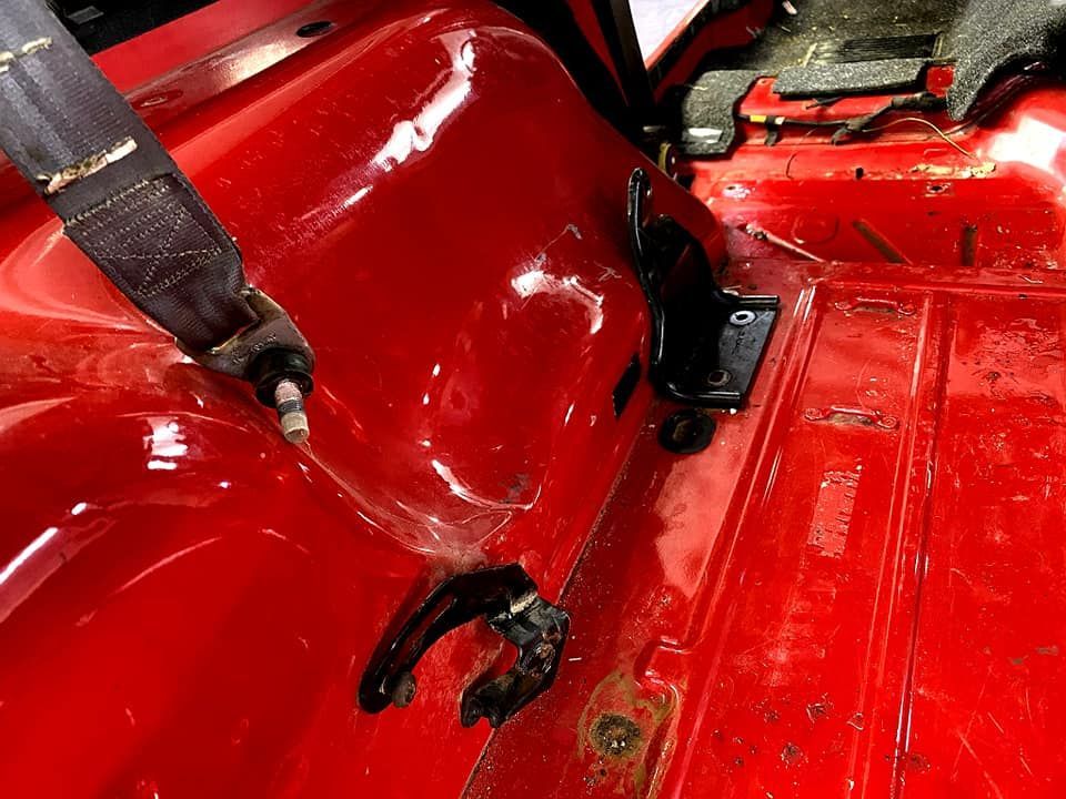 Red car interior with a black seat belt and mounting hardware.