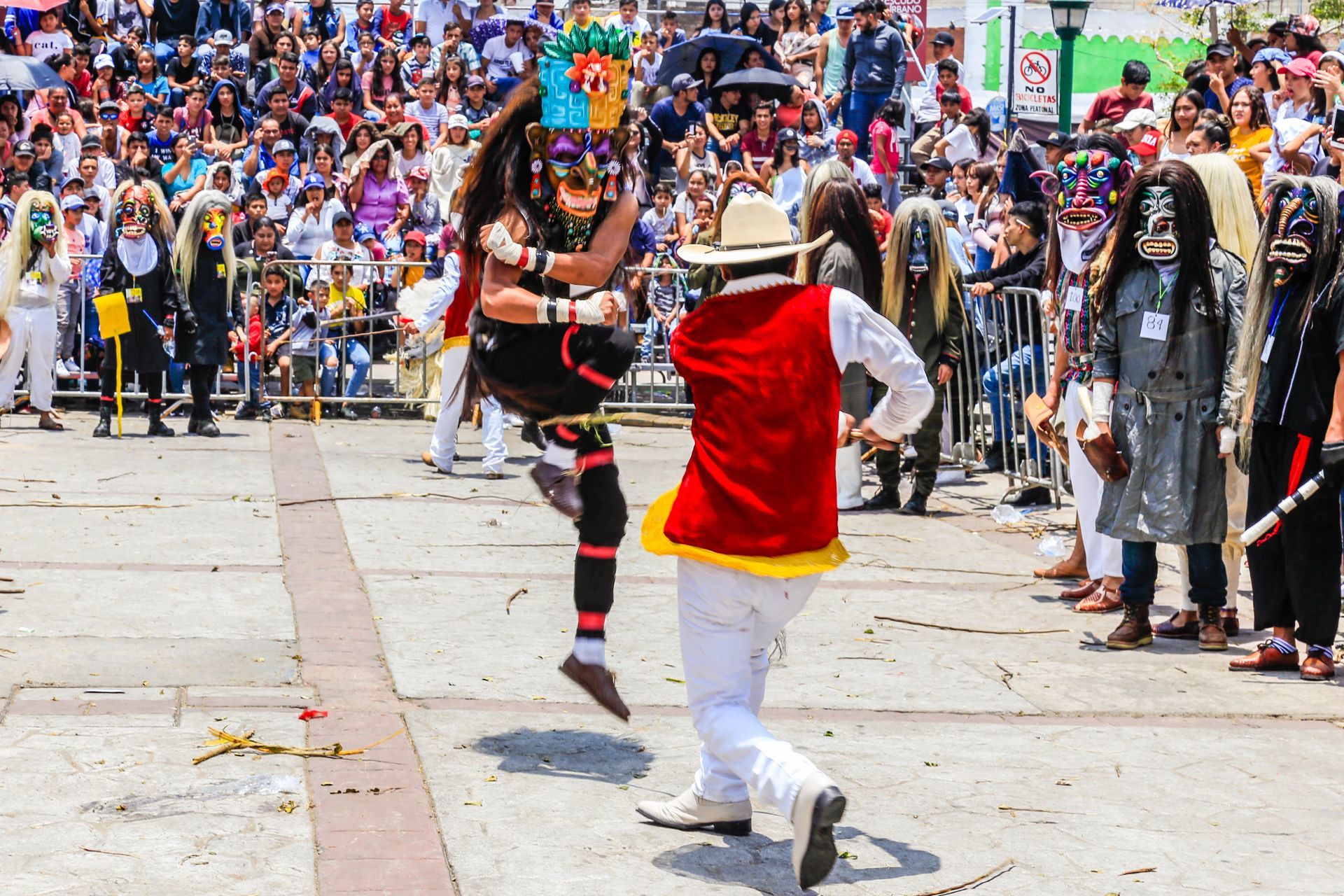 Dos bailarines disfrazados actúan en un desfile callejero ante una gran multitud que los observa desde atrás.