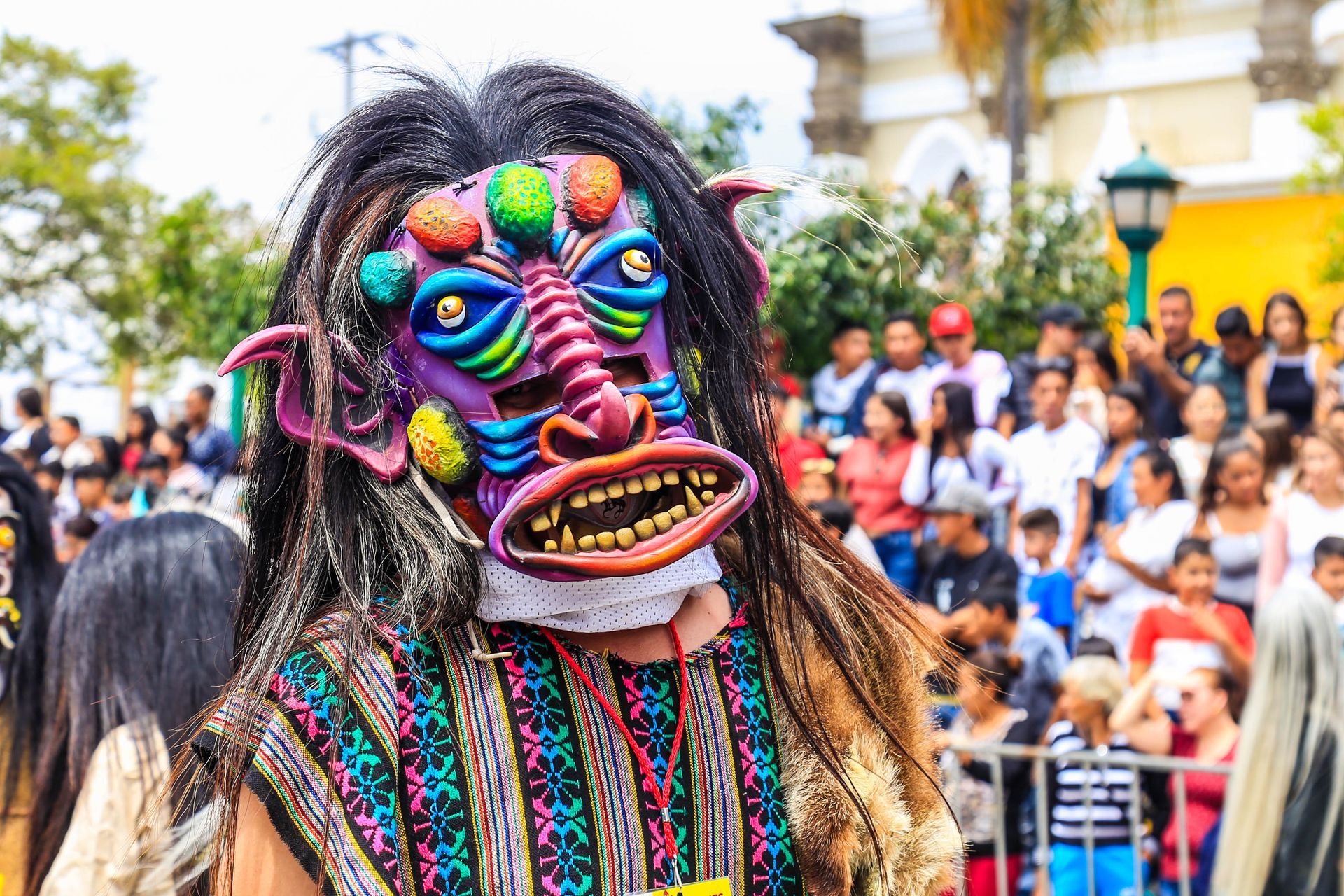 Bailarina enmascarada con colorido traje tradicional actuando ante una multitud al aire libre.