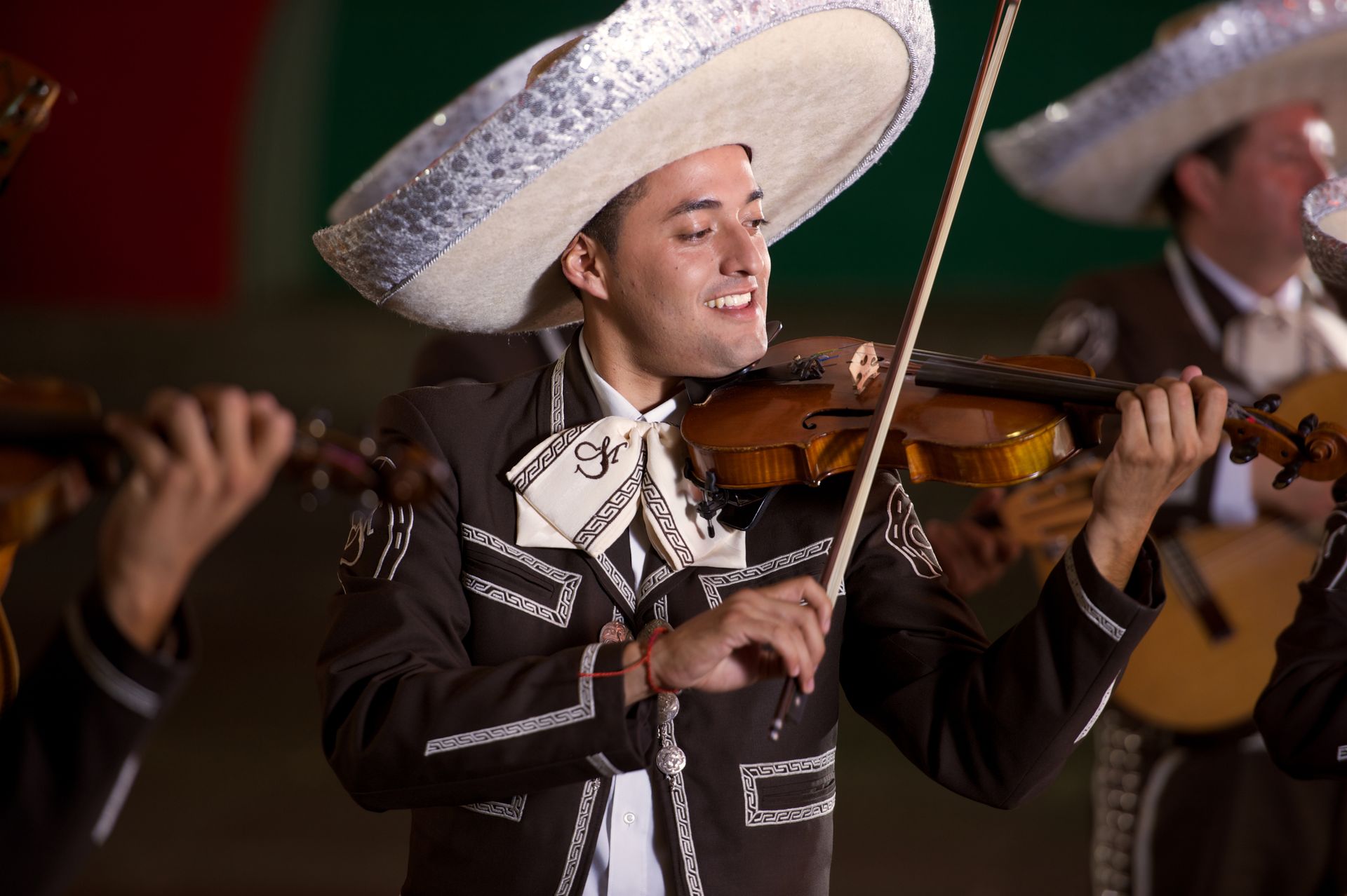 Músico mariachi con traje negro y sombrero blanco tocando el violín en el escenario.