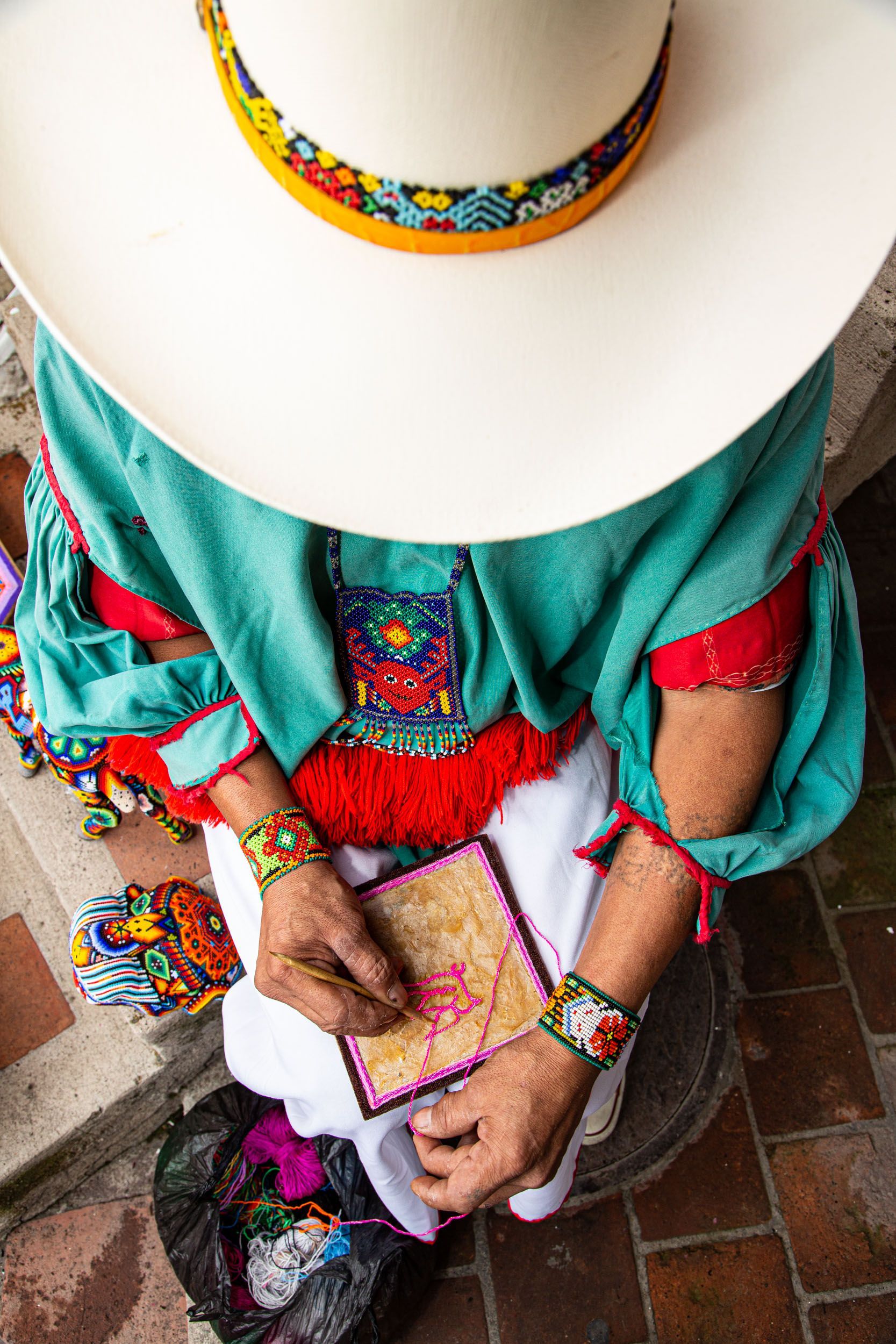 Persona con traje tradicional colorido, sentada con las manos en el regazo y un sombrero de ala ancha.