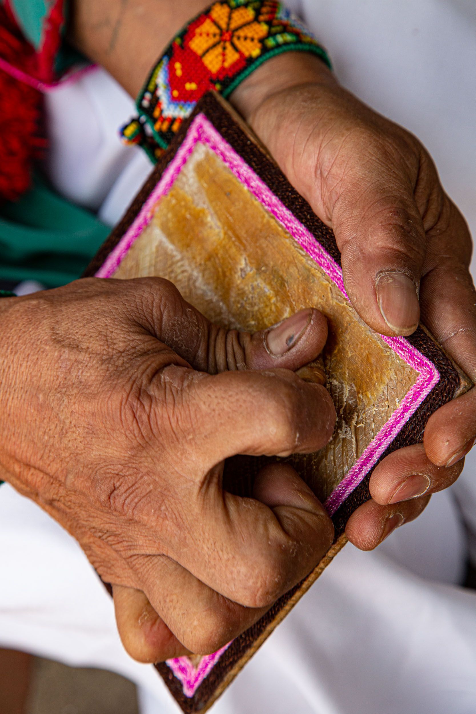 Manos sosteniendo y leyendo una pequeña libreta color canela con borde rosa y cubierta tejida de colores.