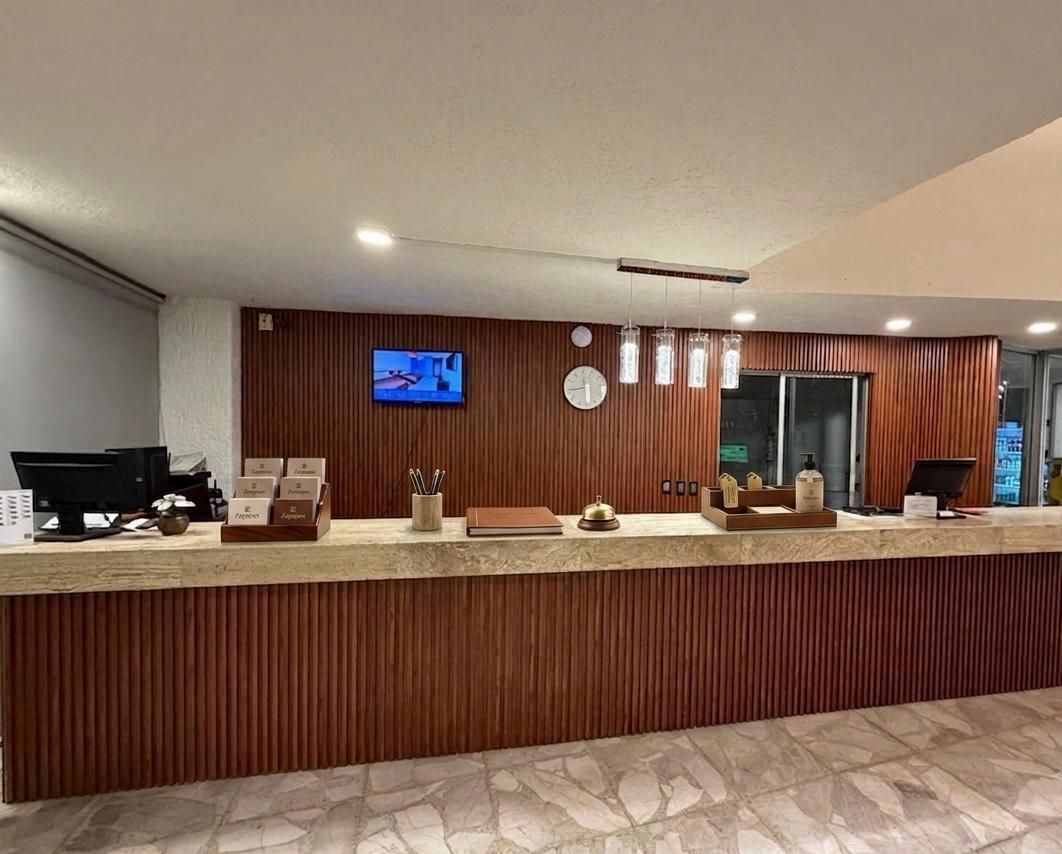 Recepción de hotel con pared de madera, encimera de piedra, reloj de pared y pequeño televisor.