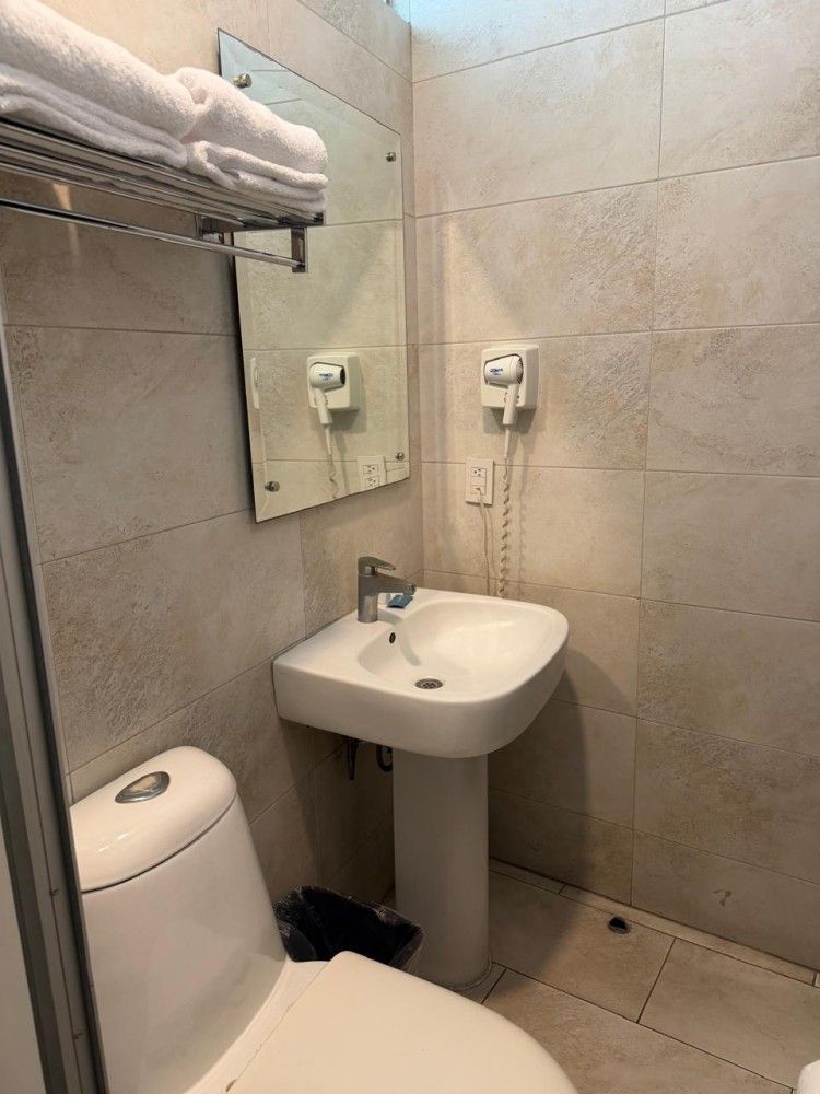 Baño pequeño con azulejos beige, lavabo, espejo, dispensadores de jabón, toallero e inodoro.